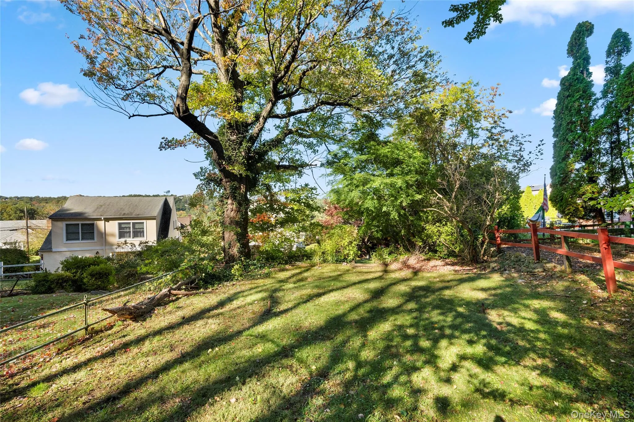 Expansive outdoor space featuring a sloped grassy lawn, mature trees, and a wooden perimeter fence Expansive outdoor space featuring a sloped grassy lawn, mature trees, and a wooden perimeter fence