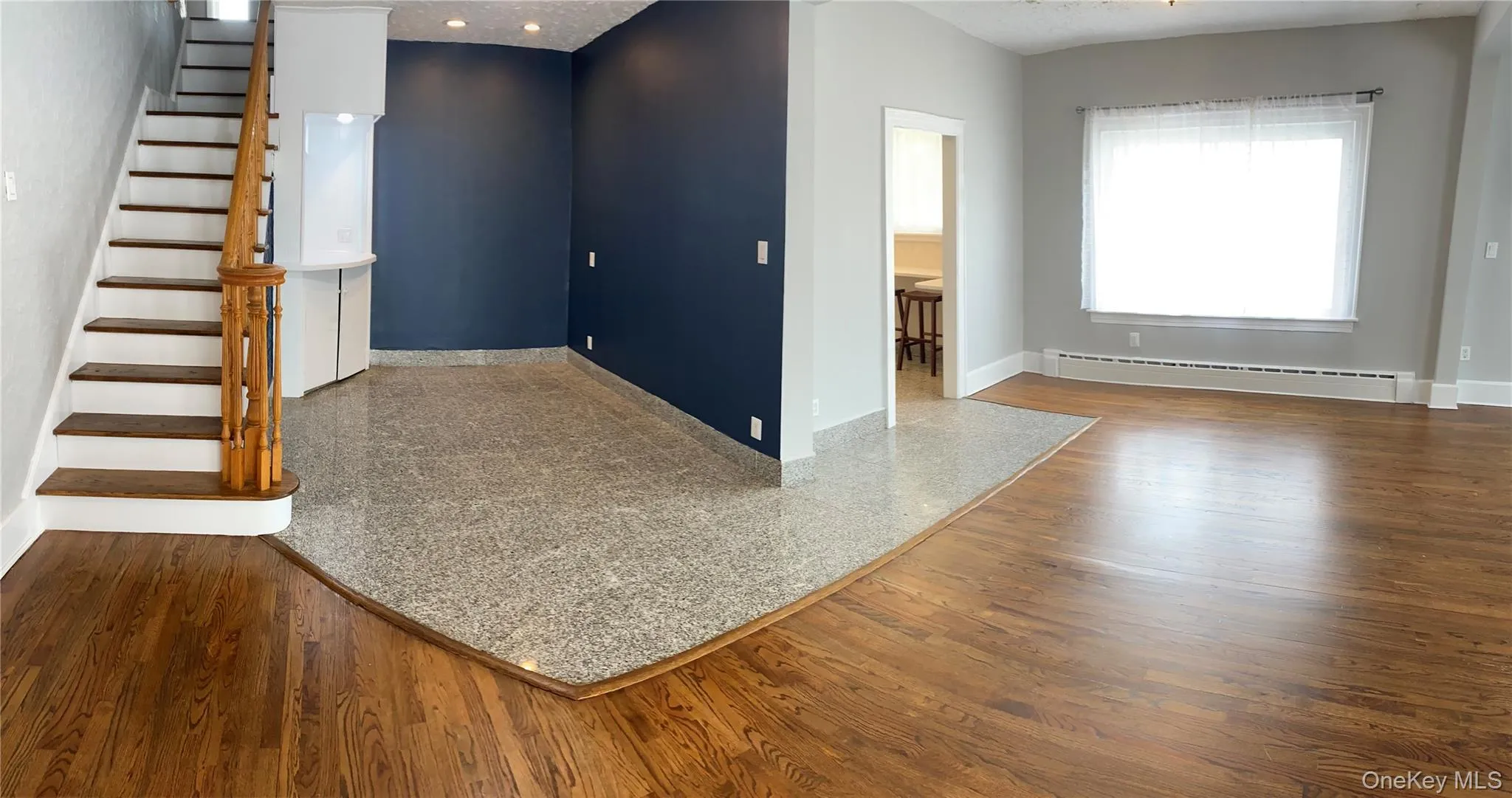 Unfurnished living room featuring a textured ceiling, baseboard heating, stairway, and wood finished floors Unfurnished living room featuring a textured ceiling, baseboard heating, stairway, and wood finished floors