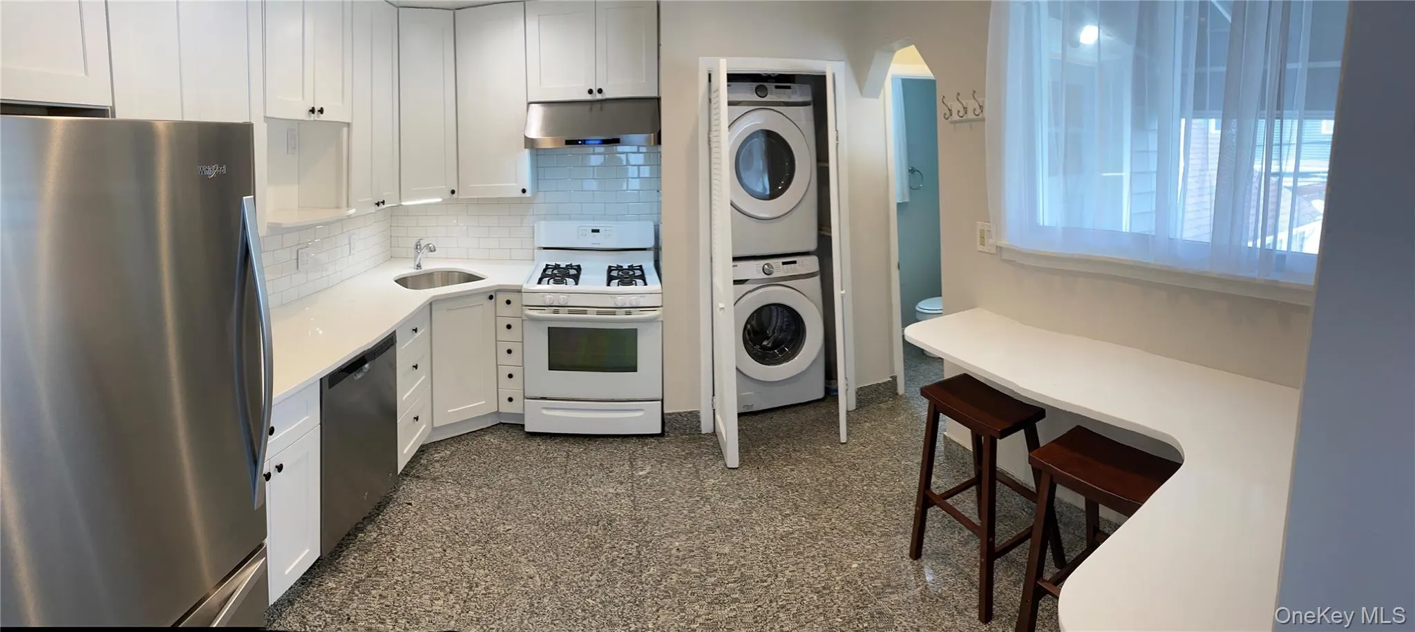 Kitchen with estacked washer and dryer, appliances with stainless steel finishes, tasteful backsplash, under cabinet range hood, and white cabinets Kitchen with estacked washer and dryer, appliances with stainless steel finishes, tasteful backsplash, under cabinet range hood, and white cabinets