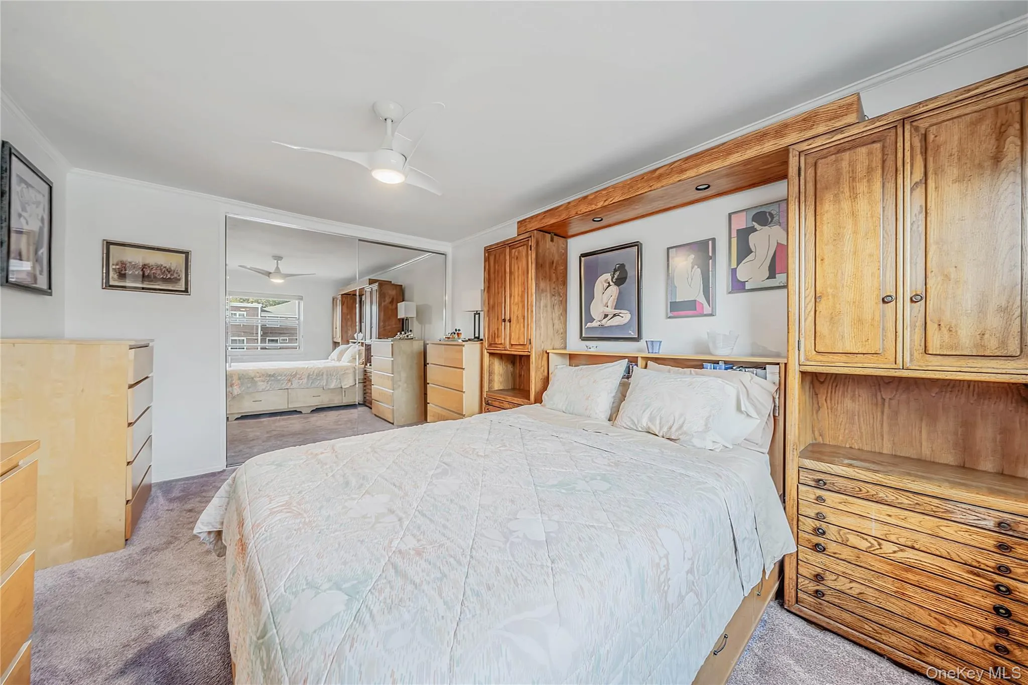 Built-in wood cabinetry featuring overhead storage, ceiling fan, and sliding mirrored closet doors Built-in wood cabinetry featuring overhead storage, ceiling fan, and sliding mirrored closet doors
