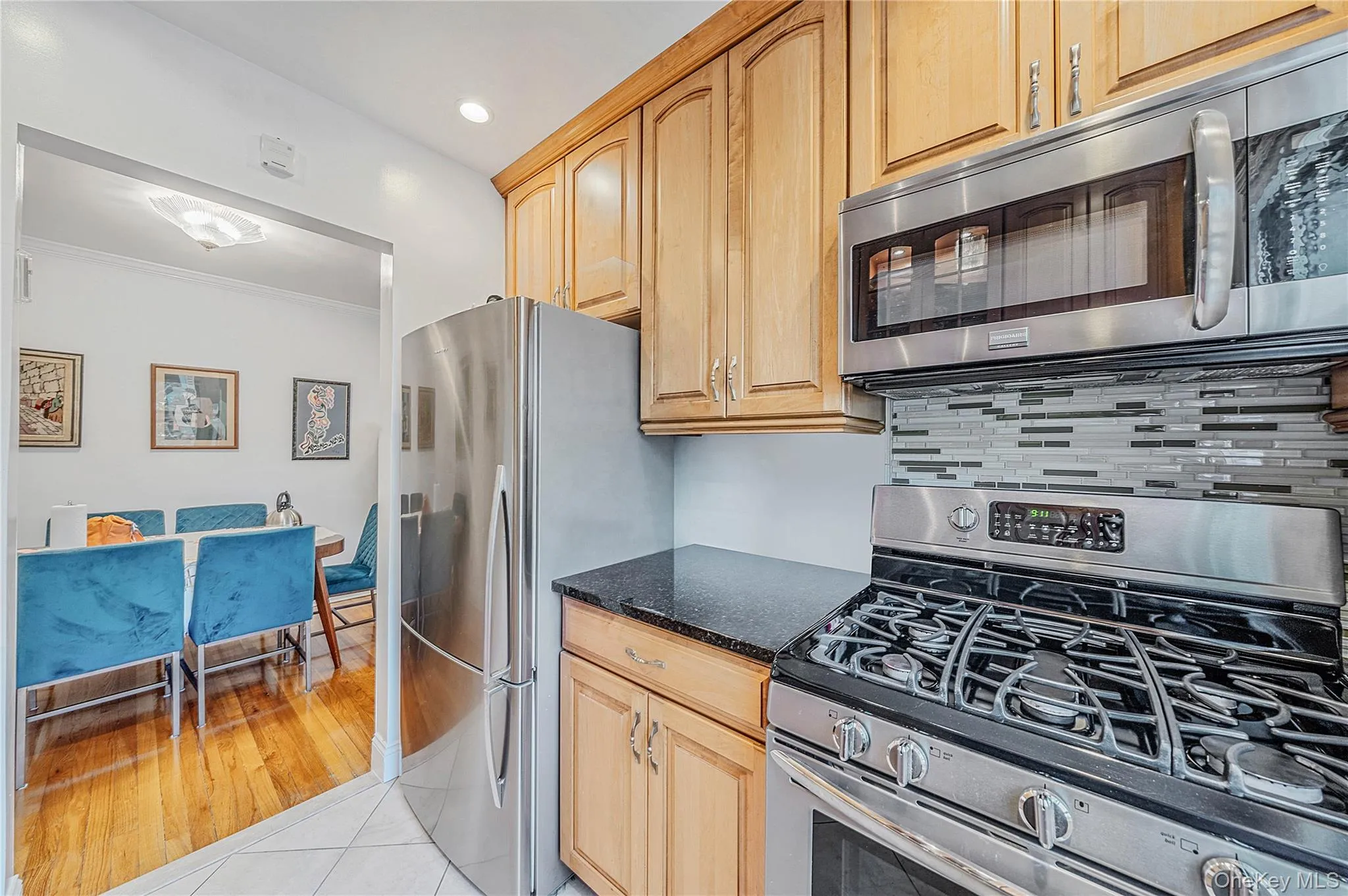 Kitchen featuring shaker-style wood cabinetry, stainless steel appliances, a multi-tone linear tile backsplash, and dark stone-finish countertops Kitchen featuring shaker-style wood cabinetry, stainless steel appliances, a multi-tone linear tile backsplash, and dark stone-finish countertops