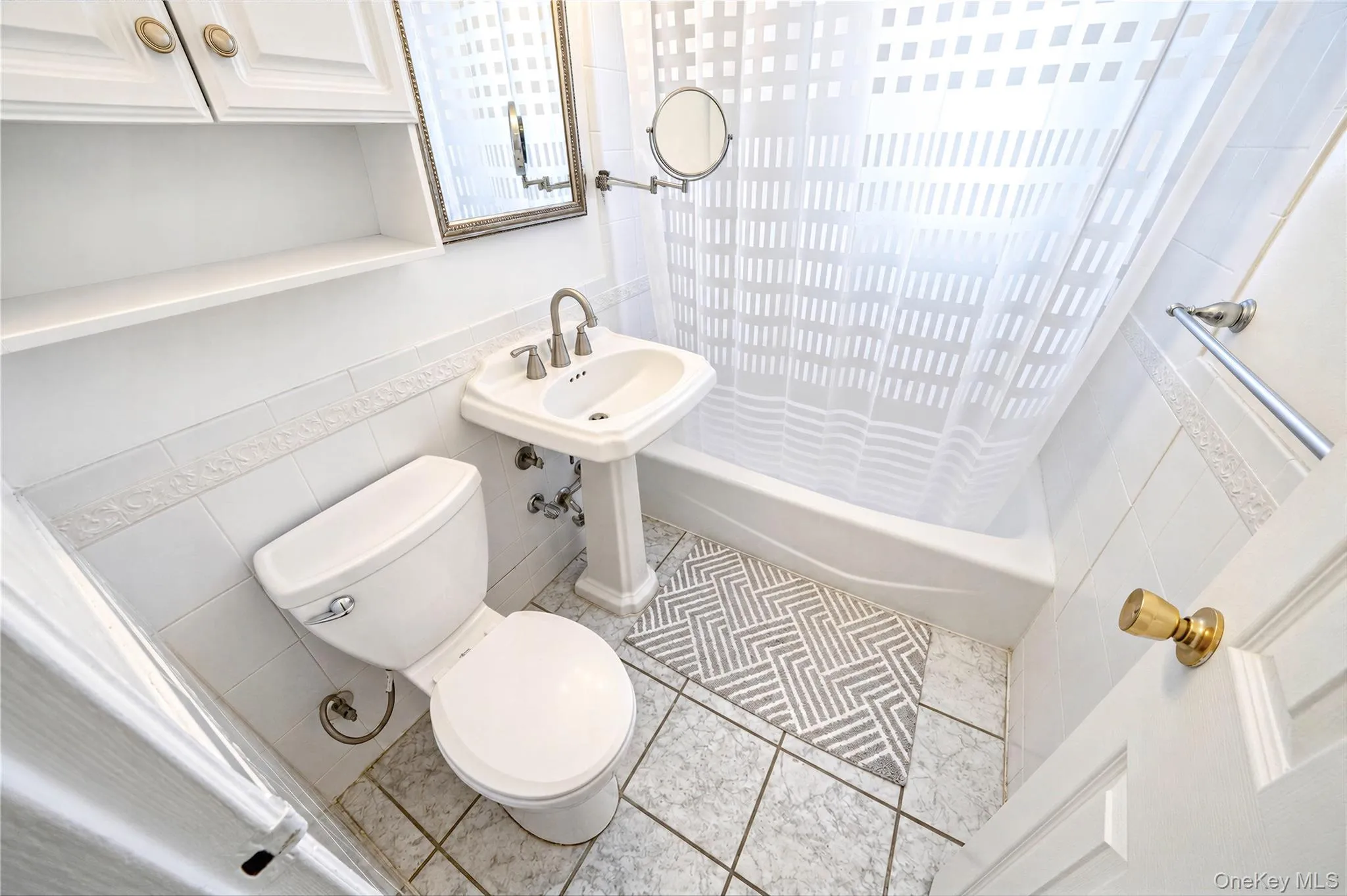 Pedestal sink with high-arch faucet, wall-mounted medicine cabinet, built-in upper cabinetry, porcelain tub with tile surround, and tile flooring Pedestal sink with high-arch faucet, wall-mounted medicine cabinet, built-in upper cabinetry, porcelain tub with tile surround, and tile flooring