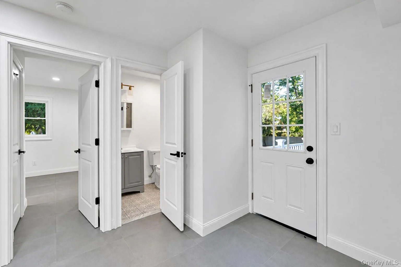 Neutral-toned ceramic tile flooring, solid-core shaker style interior doors with matte black hardware, and an exterior door with a nine-pane window insert Neutral-toned ceramic tile flooring, solid-core shaker style interior doors with matte black hardware, and an exterior door with a nine-pane window insert