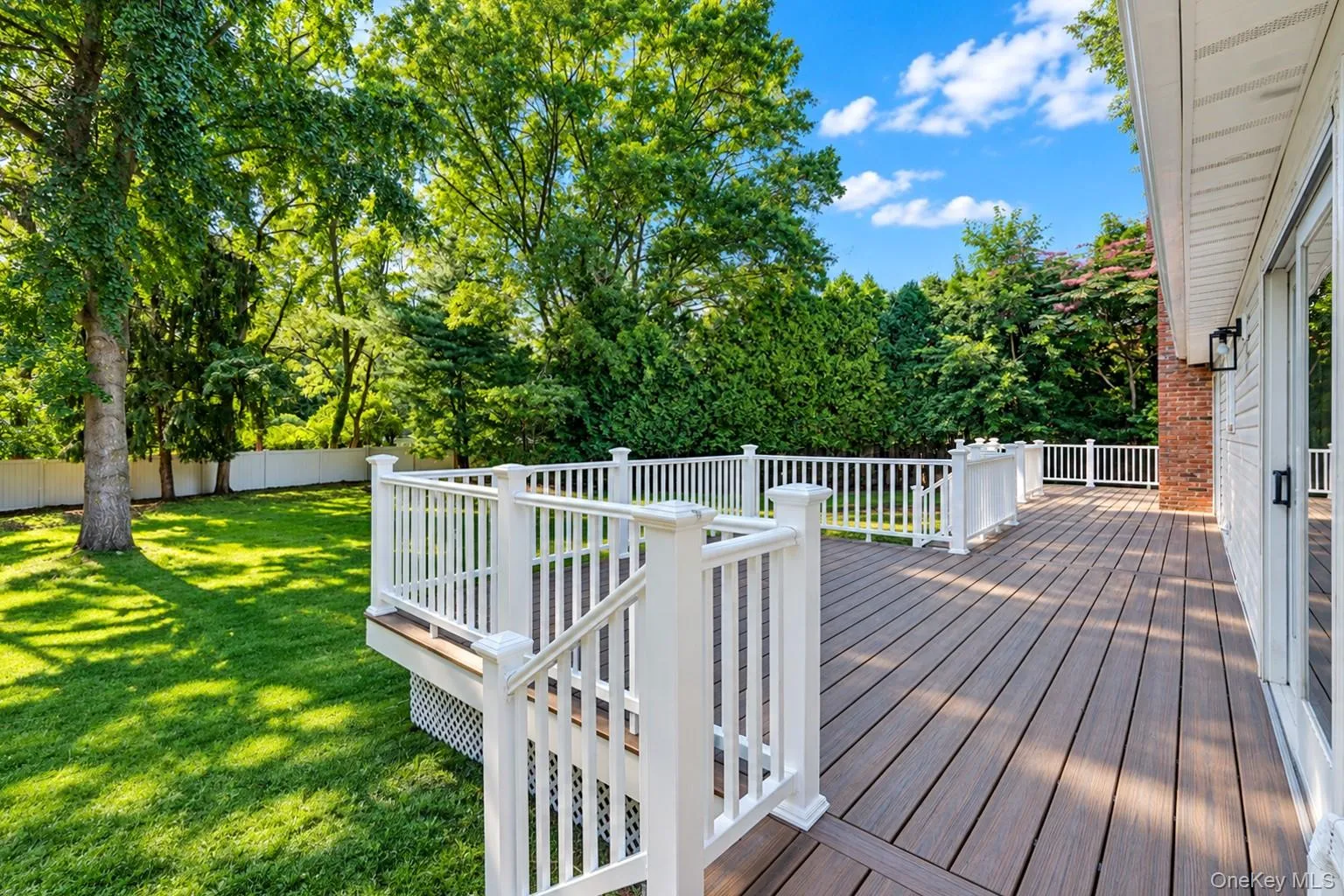 Raised composite deck with white railings, expansive grass lawn, mature trees, and white perimeter fencing Raised composite deck with white railings, expansive grass lawn, mature trees, and white perimeter fencing