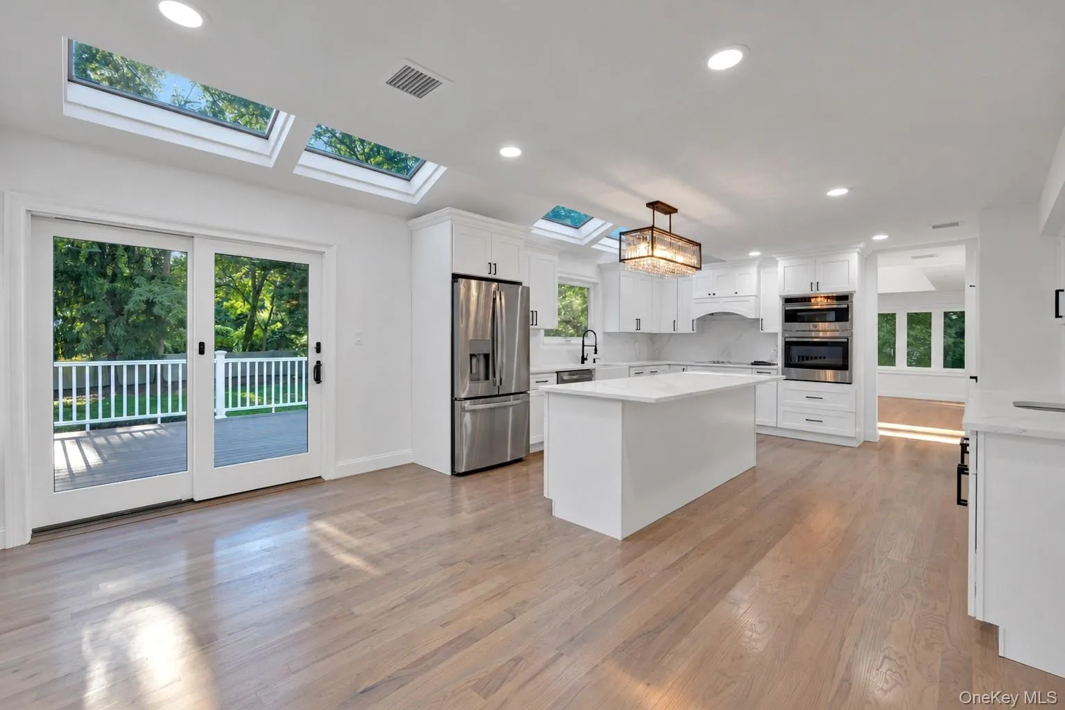 Kitchen featuring white cabinetry, central island with stone-finish countertop, stainless steel appliances, recessed ceiling lighting, and multiple skylights Kitchen featuring white cabinetry, central island with stone-finish countertop, stainless steel appliances, recessed ceiling lighting, and multiple skylights