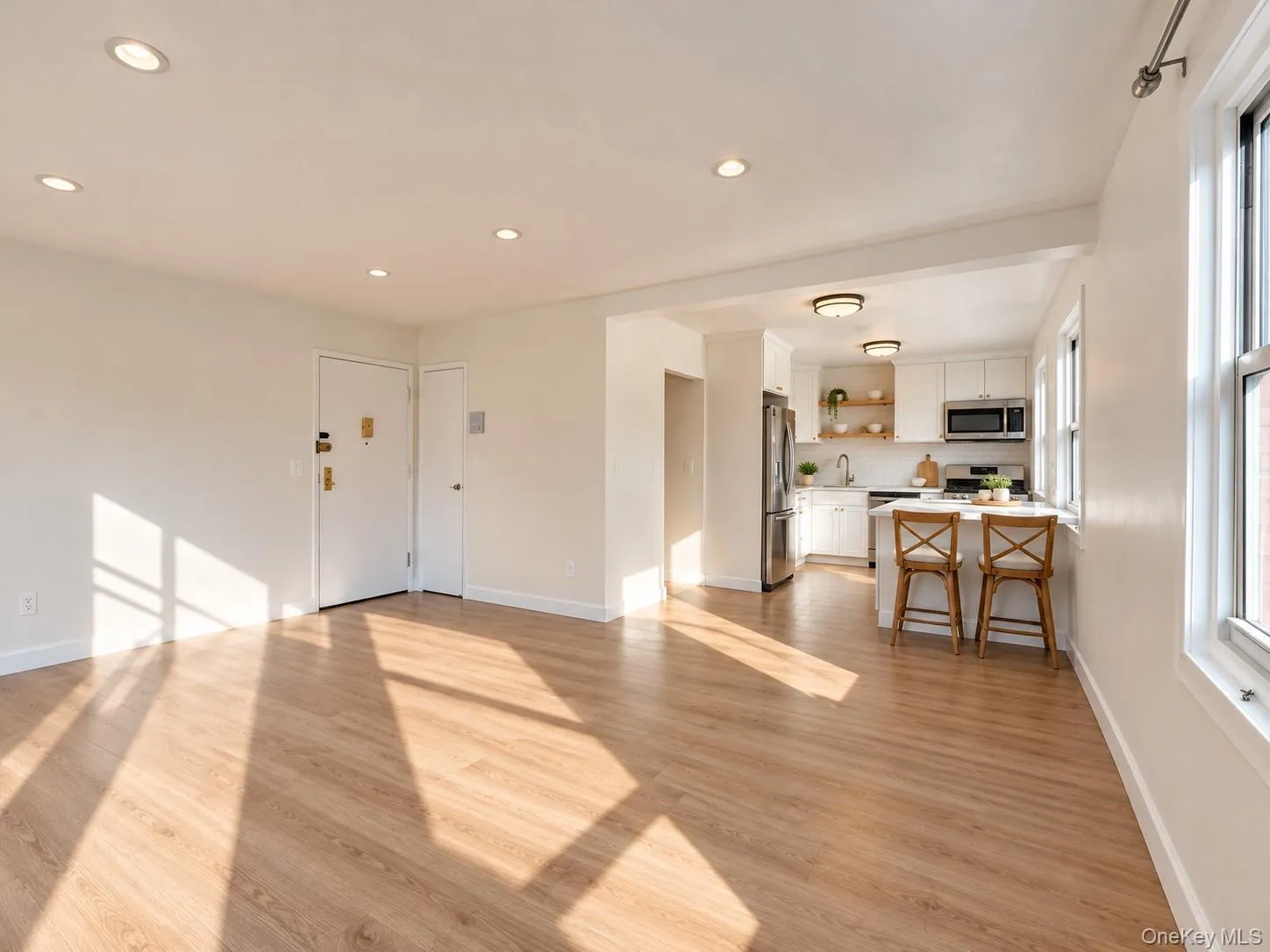 Wood-finish flooring, recessed lighting, white cabinetry, stainless steel appliances, and a kitchen island with seating Wood-finish flooring, recessed lighting, white cabinetry, stainless steel appliances, and a kitchen island with seating