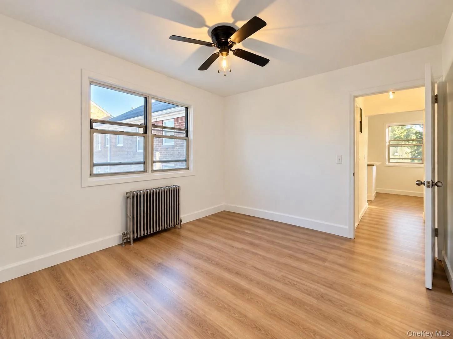 Room featuring wood-finish flooring, a multi-pane window, a metal radiator, and a central ceiling fan with an integrated light fixture Room featuring wood-finish flooring, a multi-pane window, a metal radiator, and a central ceiling fan with an integrated light fixture