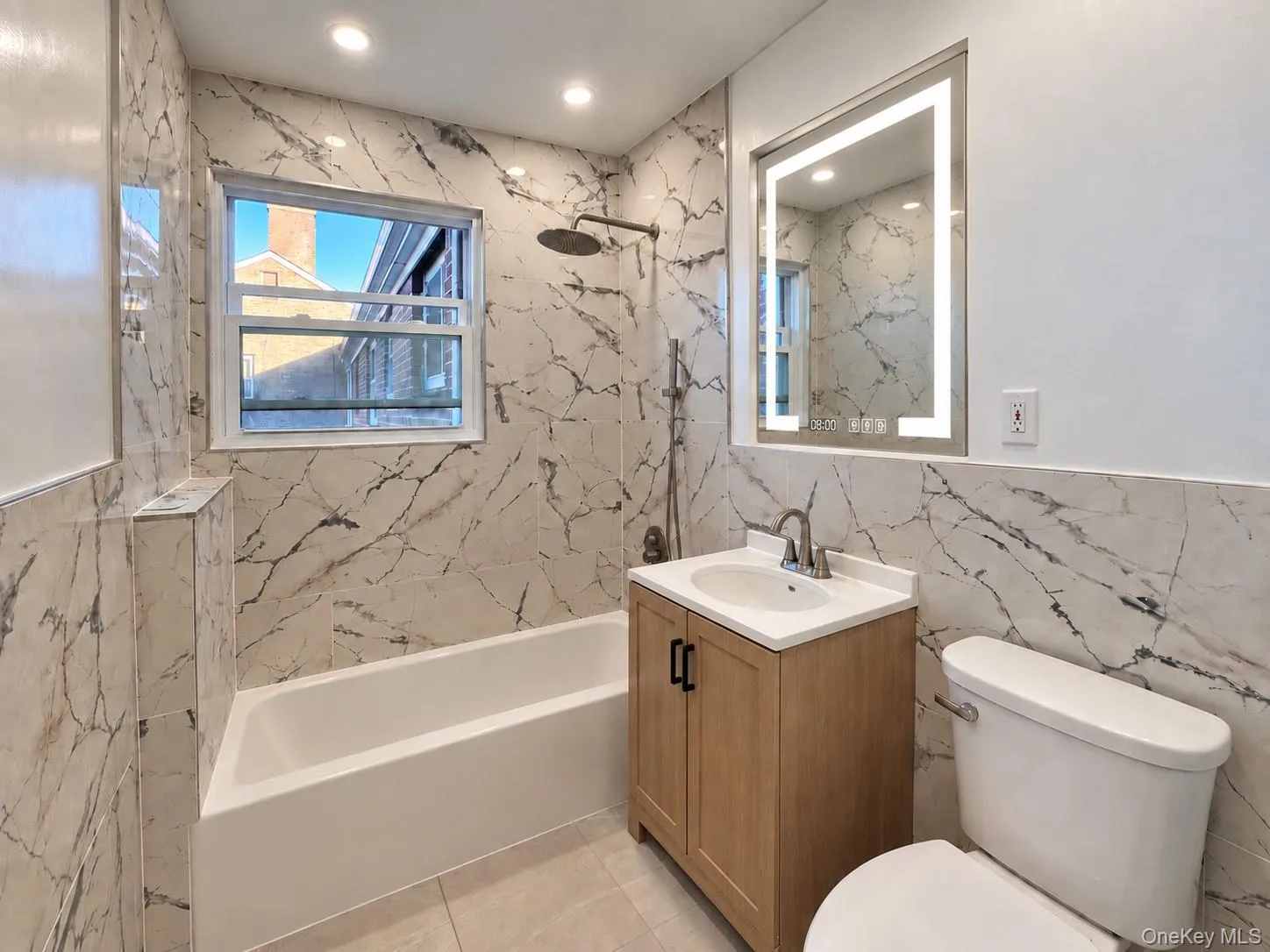 Full-height veined tile wall surfacing, built-in tub with rain-style showerhead, wood-finish vanity with stone-composite countertop, and integrated LED-lit vanity mirror Full-height veined tile wall surfacing, built-in tub with rain-style showerhead, wood-finish vanity with stone-composite countertop, and integrated LED-lit vanity mirror