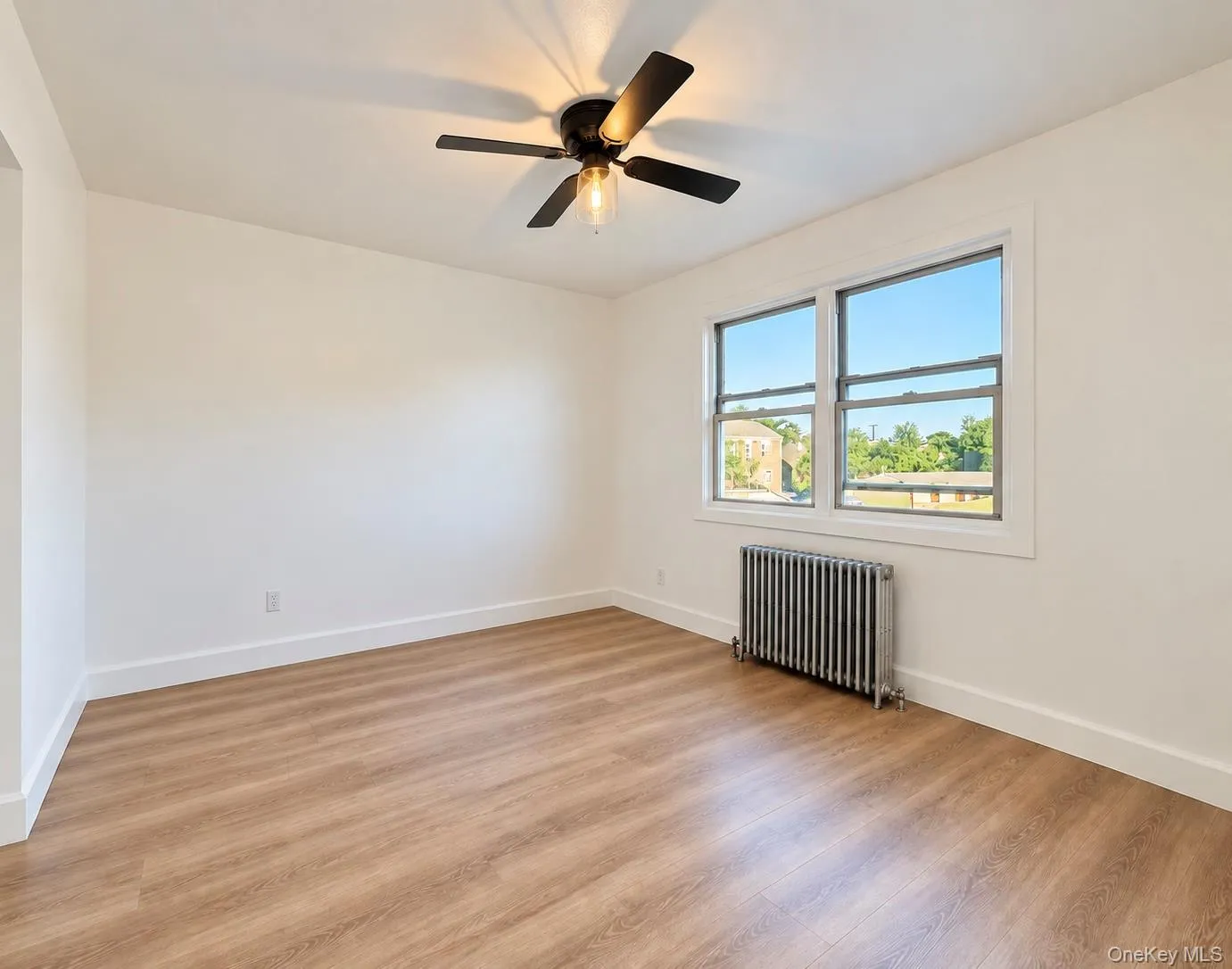 Interior space featuring wood-finish flooring, a ceiling fan with integrated lighting, dual-pane windows, and a metal radiator Interior space featuring wood-finish flooring, a ceiling fan with integrated lighting, dual-pane windows, and a metal radiator