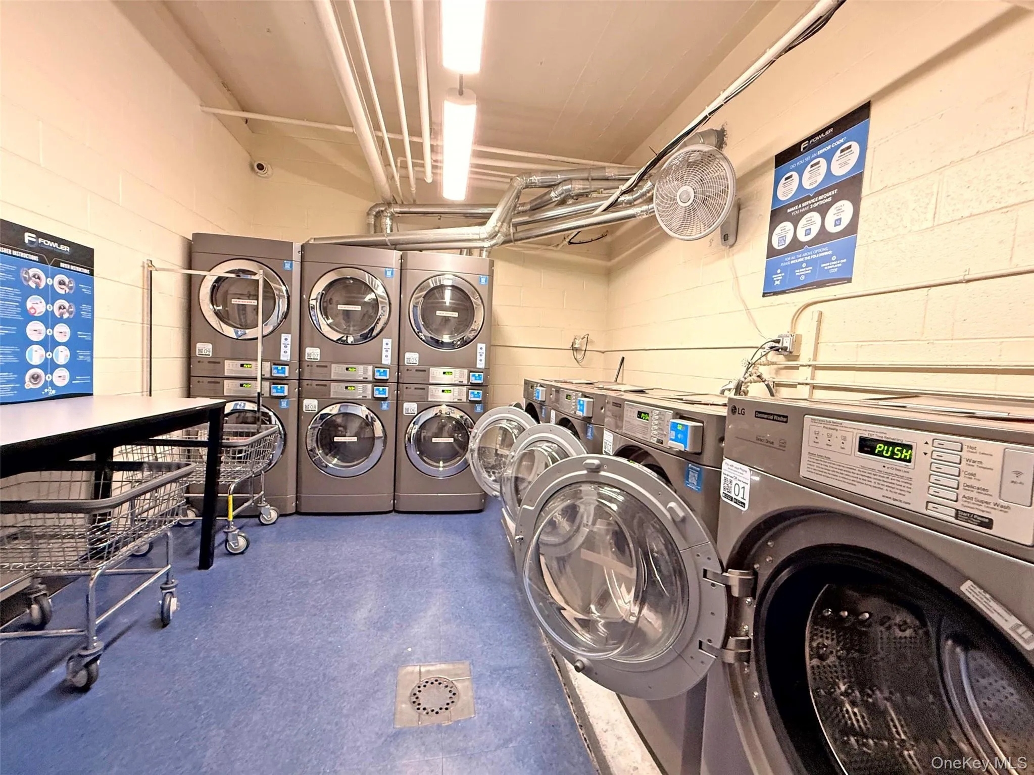 Laundry facility featuring multiple front-loading industrial washers and dryers, durable flooring, integrated floor drainage, and overhead lighting Laundry facility featuring multiple front-loading industrial washers and dryers, durable flooring, integrated floor drainage, and overhead lighting