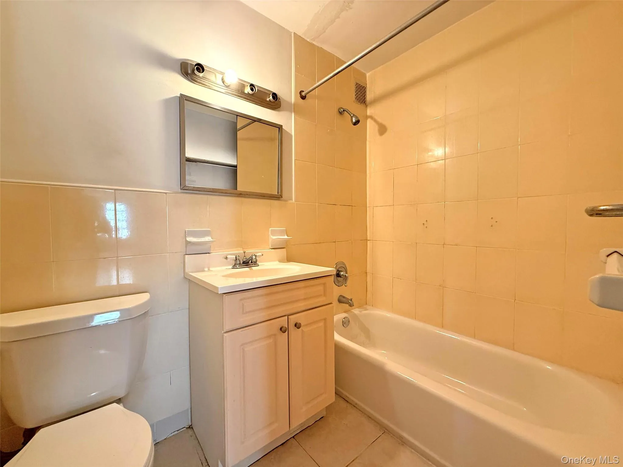 Bathroom featuring a porcelain vanity with a rectangular sink, wall-mounted medicine cabinet, tri-light fixture, tub-shower combination with tiled surround, and ceramic tile flooring Bathroom featuring a porcelain vanity with a rectangular sink, wall-mounted medicine cabinet, tri-light fixture, tub-shower combination with tiled surround, and ceramic tile flooring