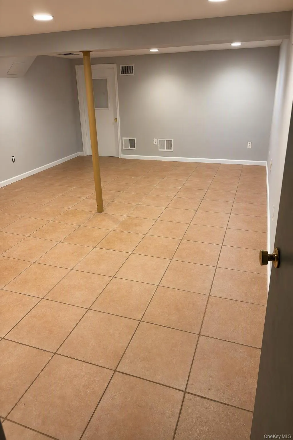 Finished space basement featuring large-format ceramic tile flooring, neutral wall paint, and recessed lighting Finished space basement featuring large-format ceramic tile flooring, neutral wall paint, and recessed lighting