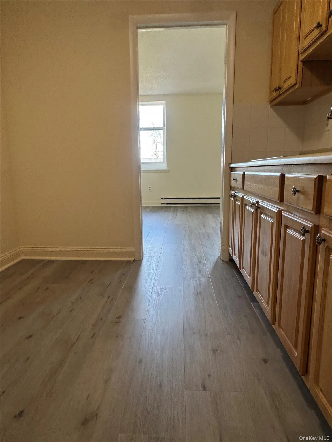 Kitchen featuring brown cabinetry, dark wood-style flooring, light countertops, and a baseboard heating unit Kitchen featuring brown cabinetry, dark wood-style flooring, light countertops, and a baseboard heating unit