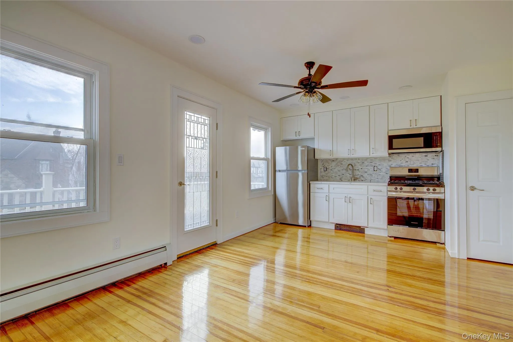 Kitchen with a baseboard heating unit, white cabinetry, stainless steel appliances, light wood-style floors, and decorative backsplash Kitchen with a baseboard heating unit, white cabinetry, stainless steel appliances, light wood-style floors, and decorative backsplash