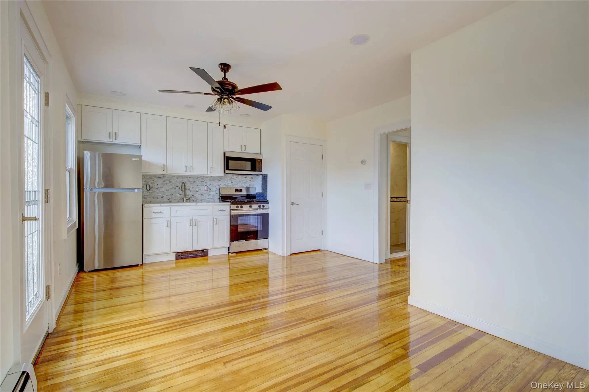 Kitchen with light wood-style flooring, backsplash, white cabinetry, appliances with stainless steel finishes, and baseboard heating Kitchen with light wood-style flooring, backsplash, white cabinetry, appliances with stainless steel finishes, and baseboard heating