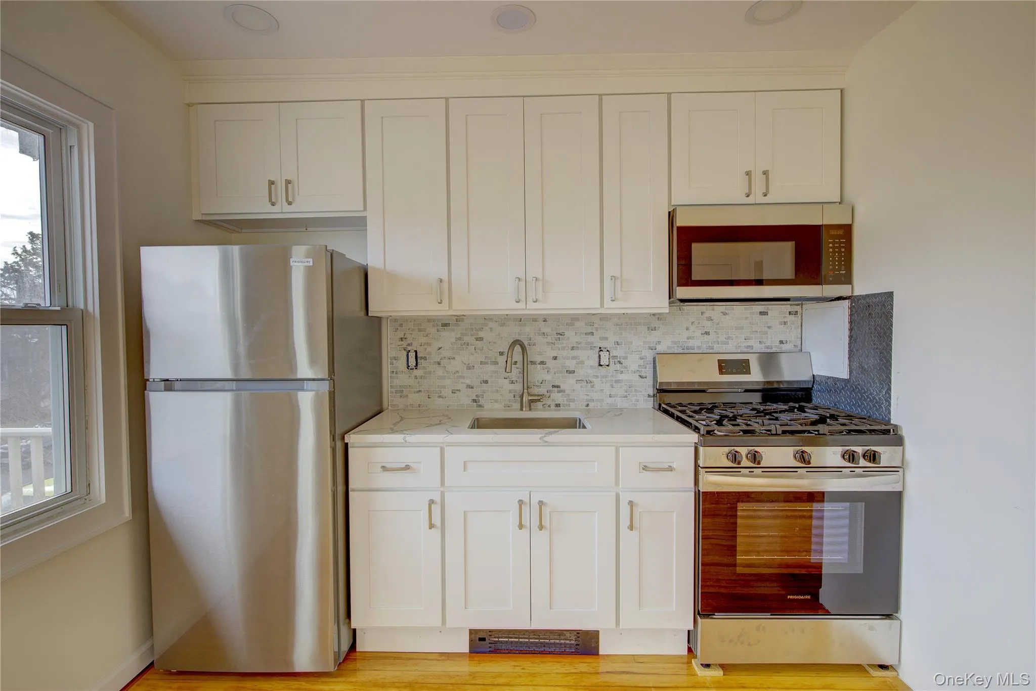 Kitchen with tasteful backsplash, light stone countertops, white cabinets, stainless steel appliances, and a sink Kitchen with tasteful backsplash, light stone countertops, white cabinets, stainless steel appliances, and a sink