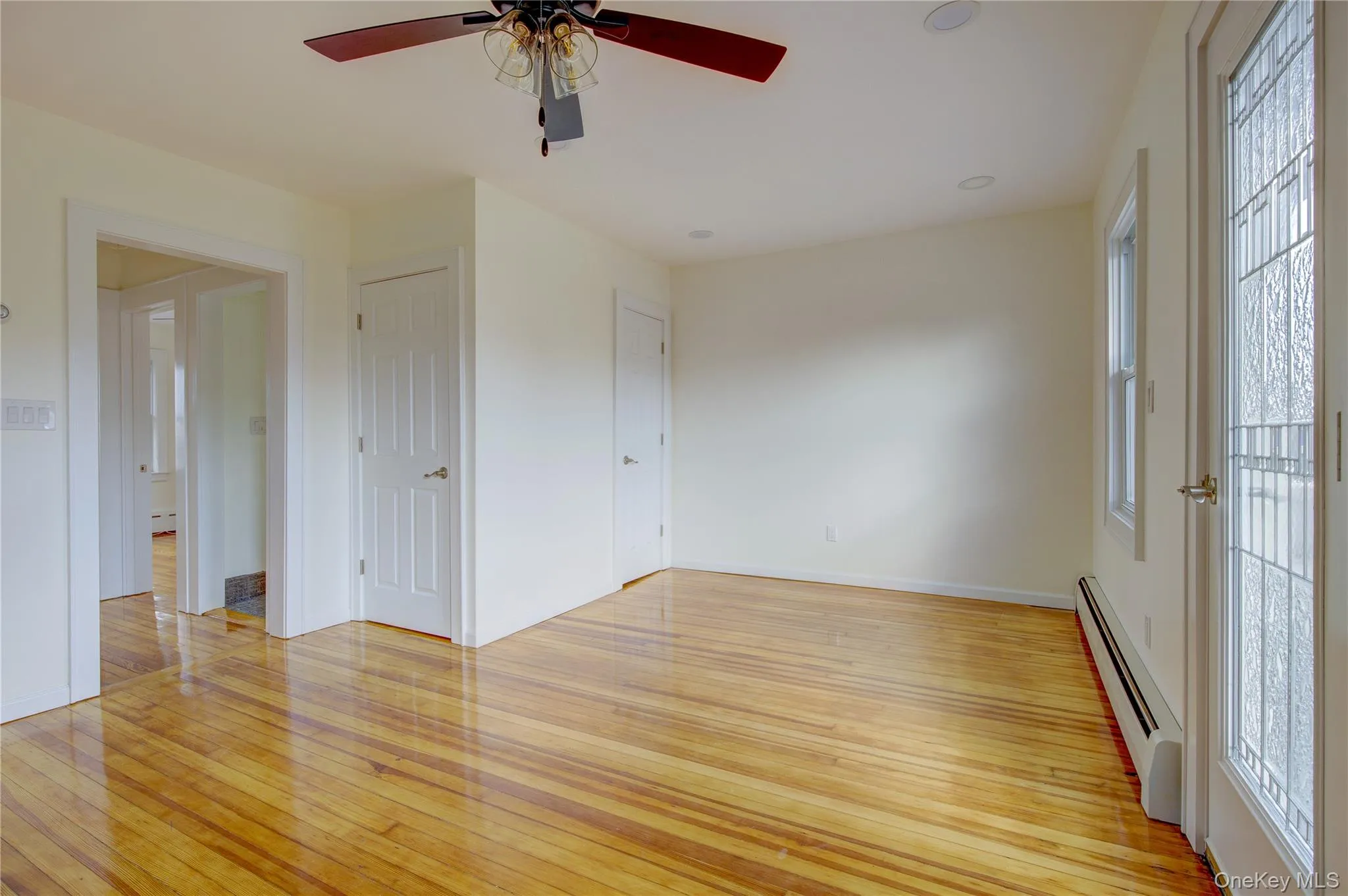 Unfurnished room featuring light wood finished floors, a baseboard heating unit, and baseboards Unfurnished room featuring light wood finished floors, a baseboard heating unit, and baseboards
