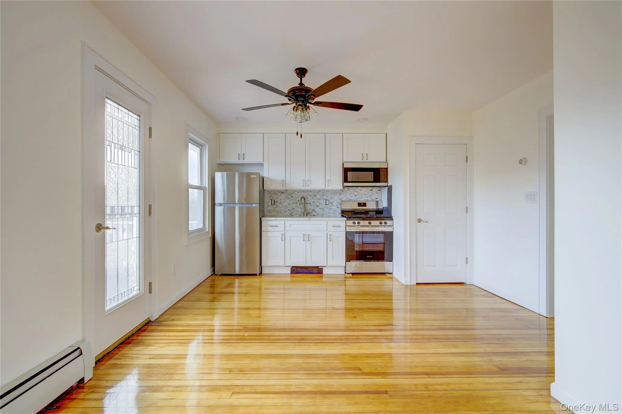 Kitchen featuring light wood finished floors, decorative backsplash, stainless steel appliances, and a baseboard radiator Kitchen featuring light wood finished floors, decorative backsplash, stainless steel appliances, and a baseboard radiator