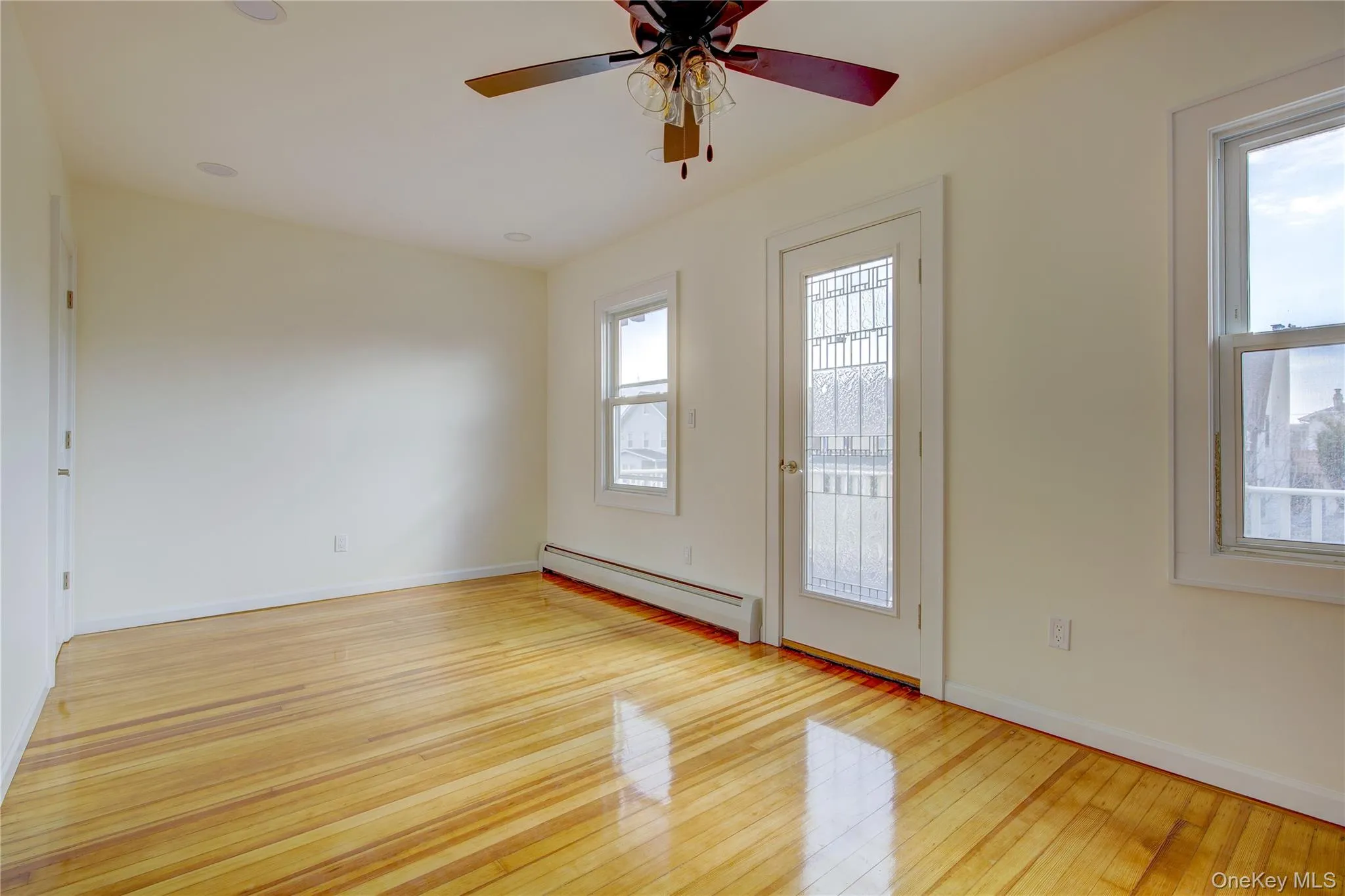 Empty room featuring a baseboard heating unit, a healthy amount of sunlight, baseboards, and hardwood / wood-style floors Empty room featuring a baseboard heating unit, a healthy amount of sunlight, baseboards, and hardwood / wood-style floors