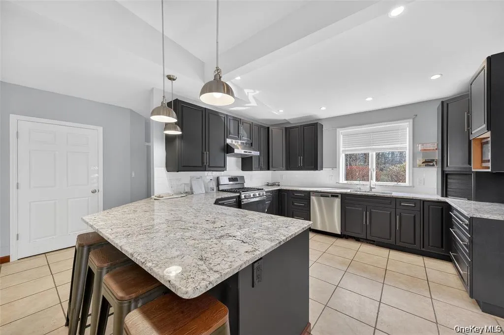 Kitchen featuring a kitchenbreakfast bar, backsplash, apeninsula, stainless steelappliances, and light stonecounters Kitchen featuring a kitchenbreakfast bar, backsplash, apeninsula, stainless steelappliances, and light stonecounters