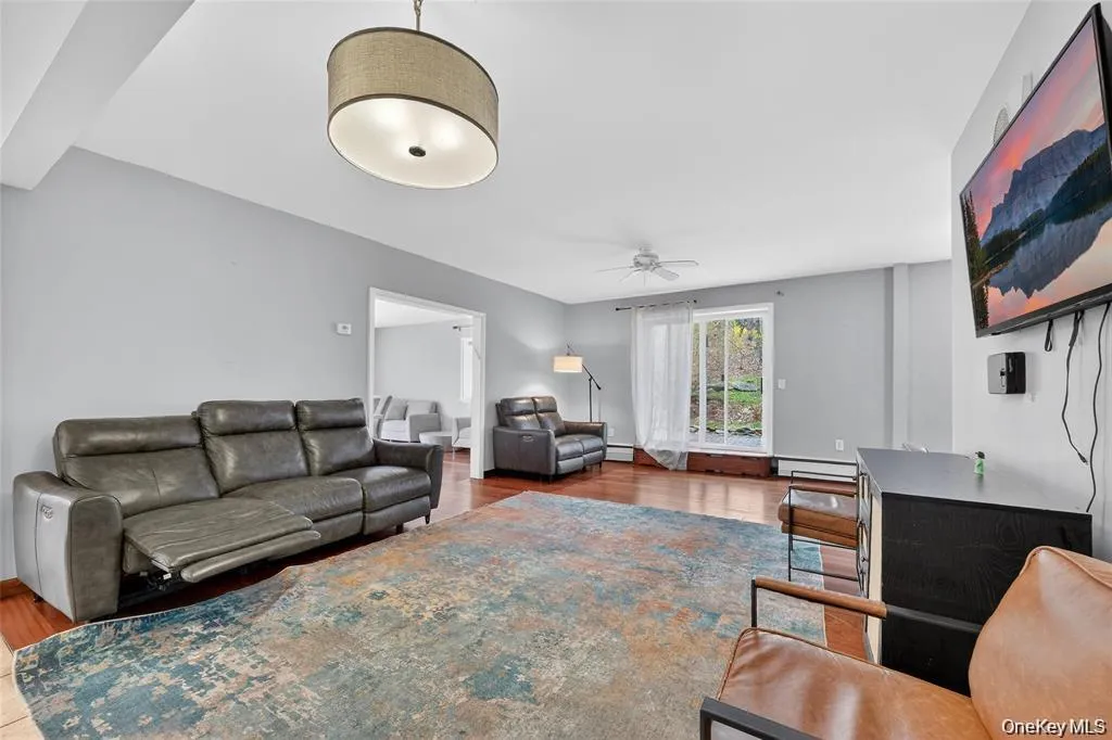 Living room featuring lightwood-type flooring, a ceiling fan, and baseboard heating Living room featuring lightwood-type flooring, a ceiling fan, and baseboard heating