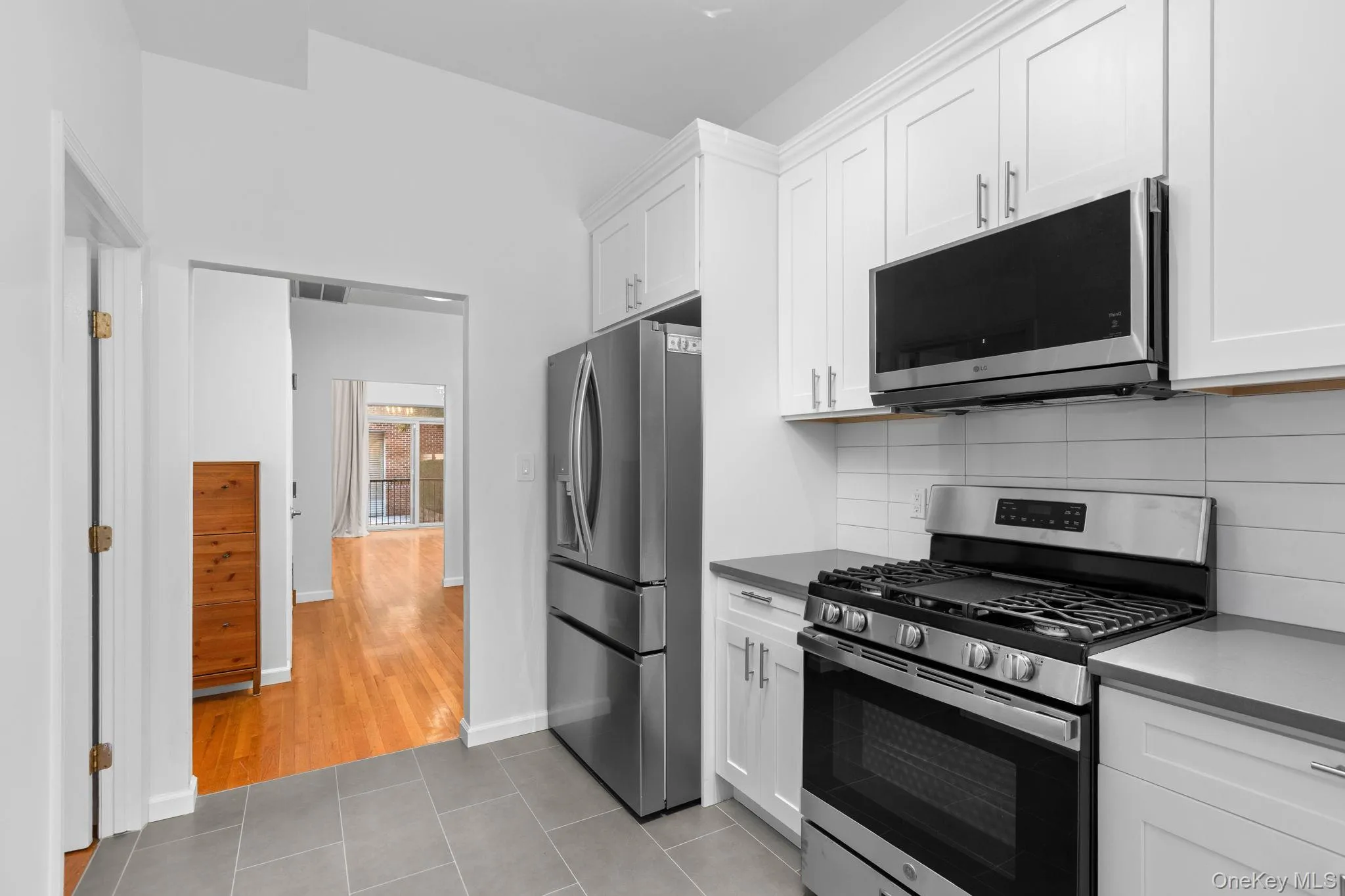 Kitchen featuring white shaker-style cabinetry, stainless steel appliances, a gas range with an over-the-range microwave, solid-surface countertops, and tiled flooring Kitchen featuring white shaker-style cabinetry, stainless steel appliances, a gas range with an over-the-range microwave, solid-surface countertops, and tiled flooring