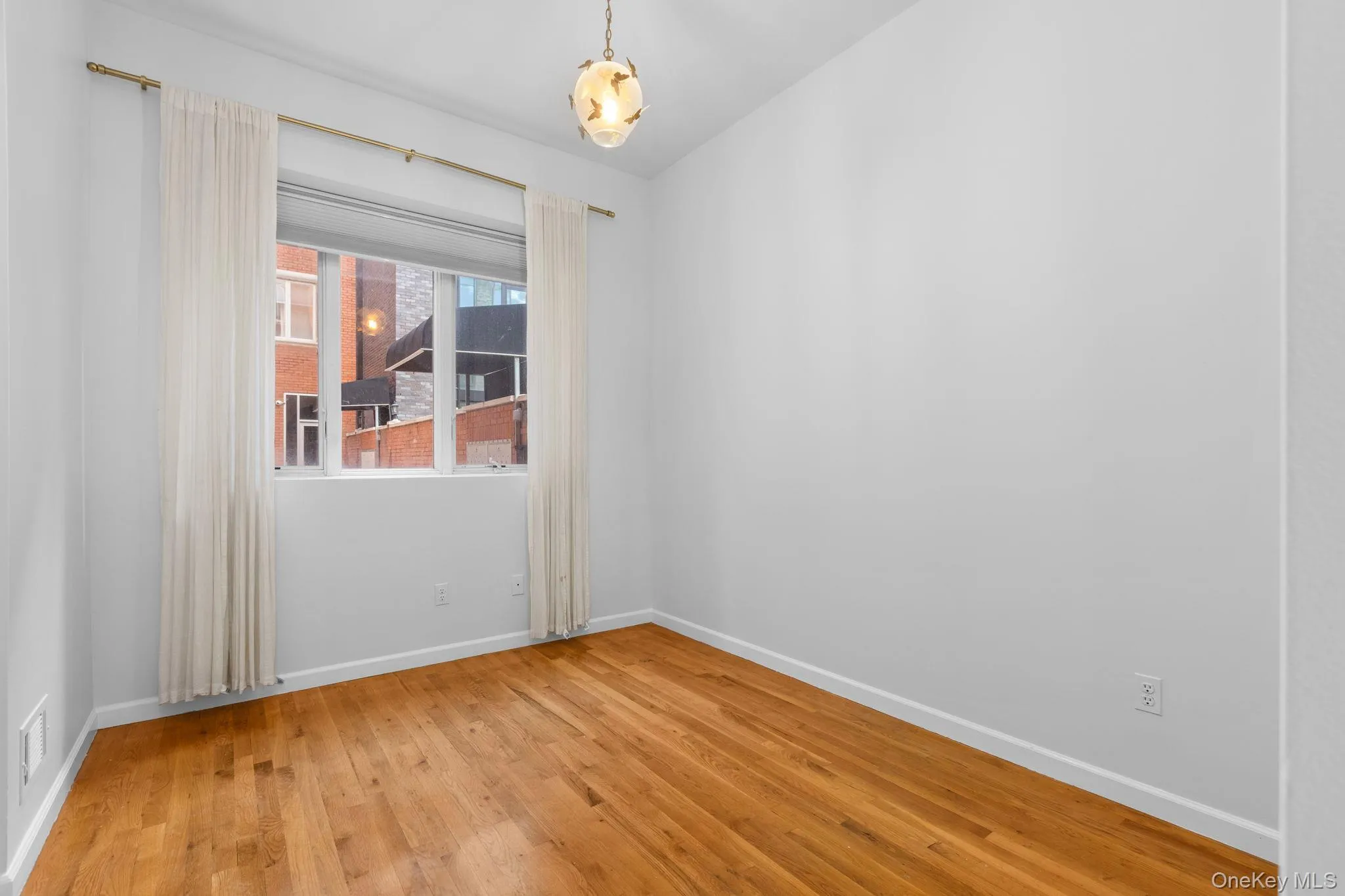 Room featuring wood-finish flooring, a multi-pane window, and a hanging pendant light fixture Room featuring wood-finish flooring, a multi-pane window, and a hanging pendant light fixture