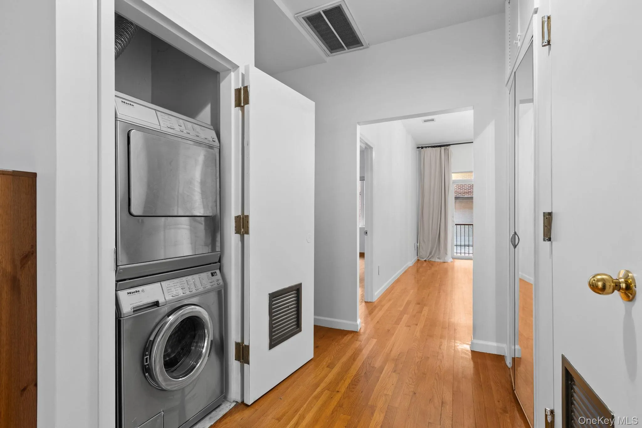 Stacked laundry unit with stainless steel appliances, wood-finish flooring, and mirrored closet doors Stacked laundry unit with stainless steel appliances, wood-finish flooring, and mirrored closet doors