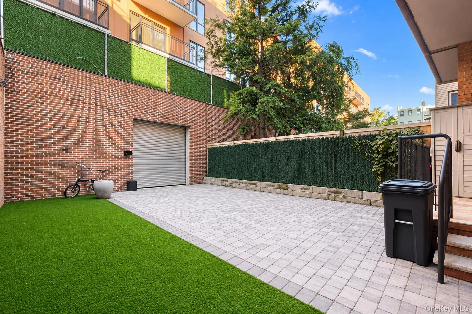 Private outdoor patio featuring brick wall construction, synthetic turf, stone paver hardscaping, with a detached garage for private parking and perimeter privacy fencing Private outdoor patio featuring brick wall construction, synthetic turf, stone paver hardscaping, with a detached garage for private parking and perimeter privacy fencing