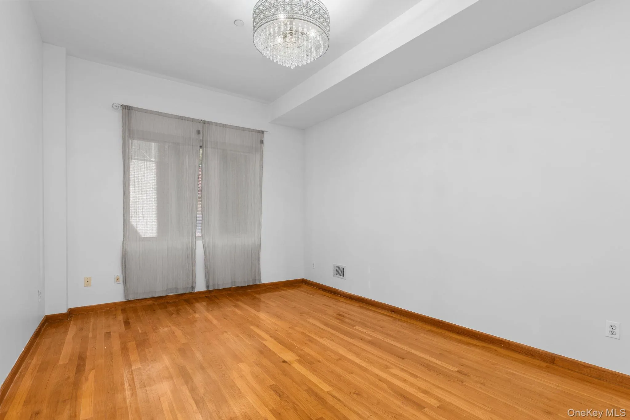Primary bedroom featuring wood-finish flooring, a decorative crystal-style chandelier, and a recessed ceiling design. Primary bedroom featuring wood-finish flooring, a decorative crystal-style chandelier, and a recessed ceiling design.