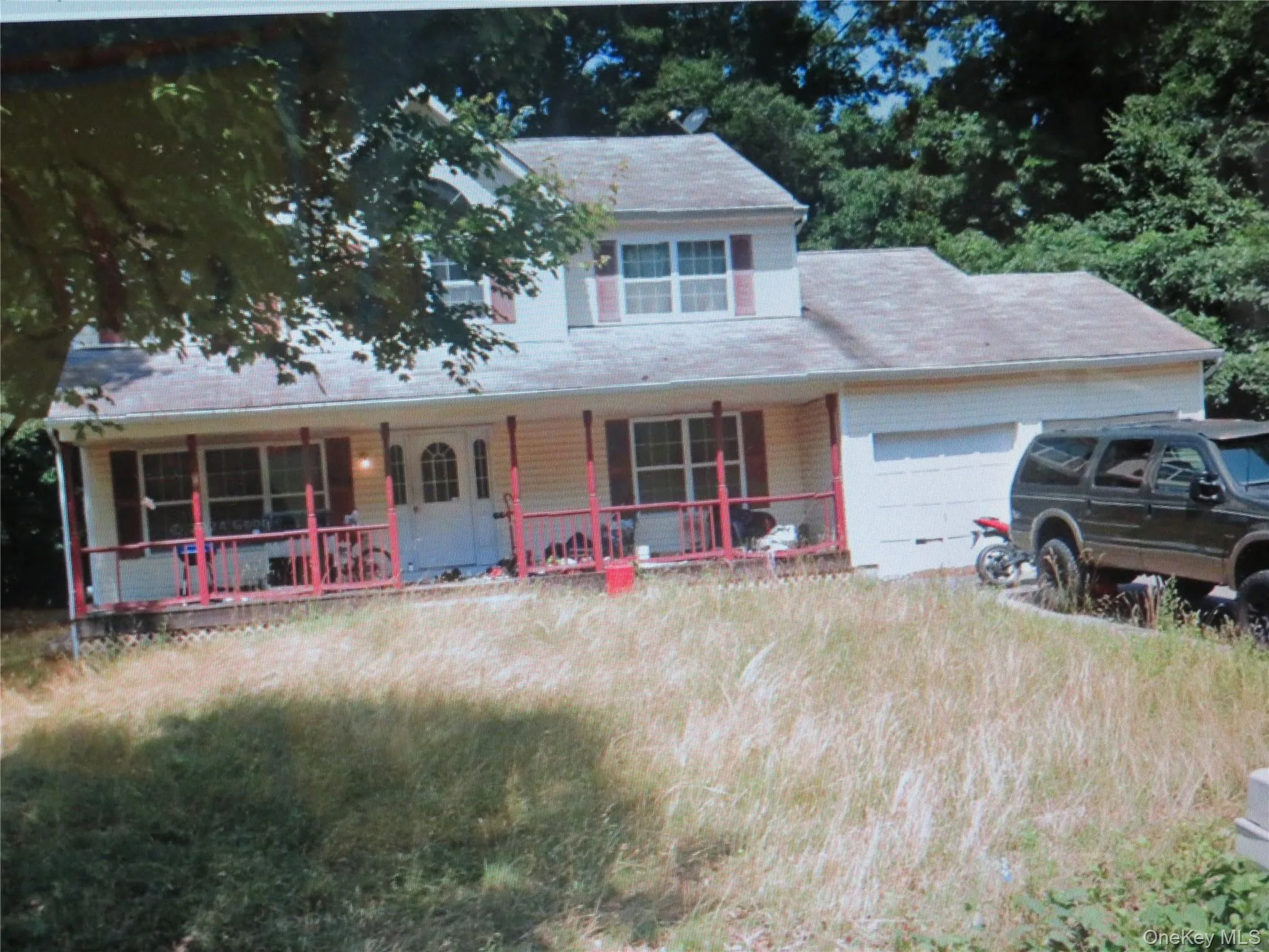 Two-story residence featuring light-colored siding, a covered front porch with a railing, an arched window, and an attached garage Two-story residence featuring light-colored siding, a covered front porch with a railing, an arched window, and an attached garage