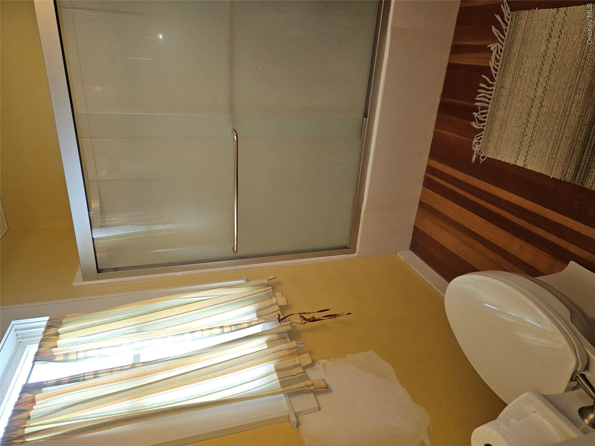 Bathroom featuring wood-finish flooring, a white porcelain toilet, and a shower enclosure with sliding glass doors and a metal frame Bathroom featuring wood-finish flooring, a white porcelain toilet, and a shower enclosure with sliding glass doors and a metal frame