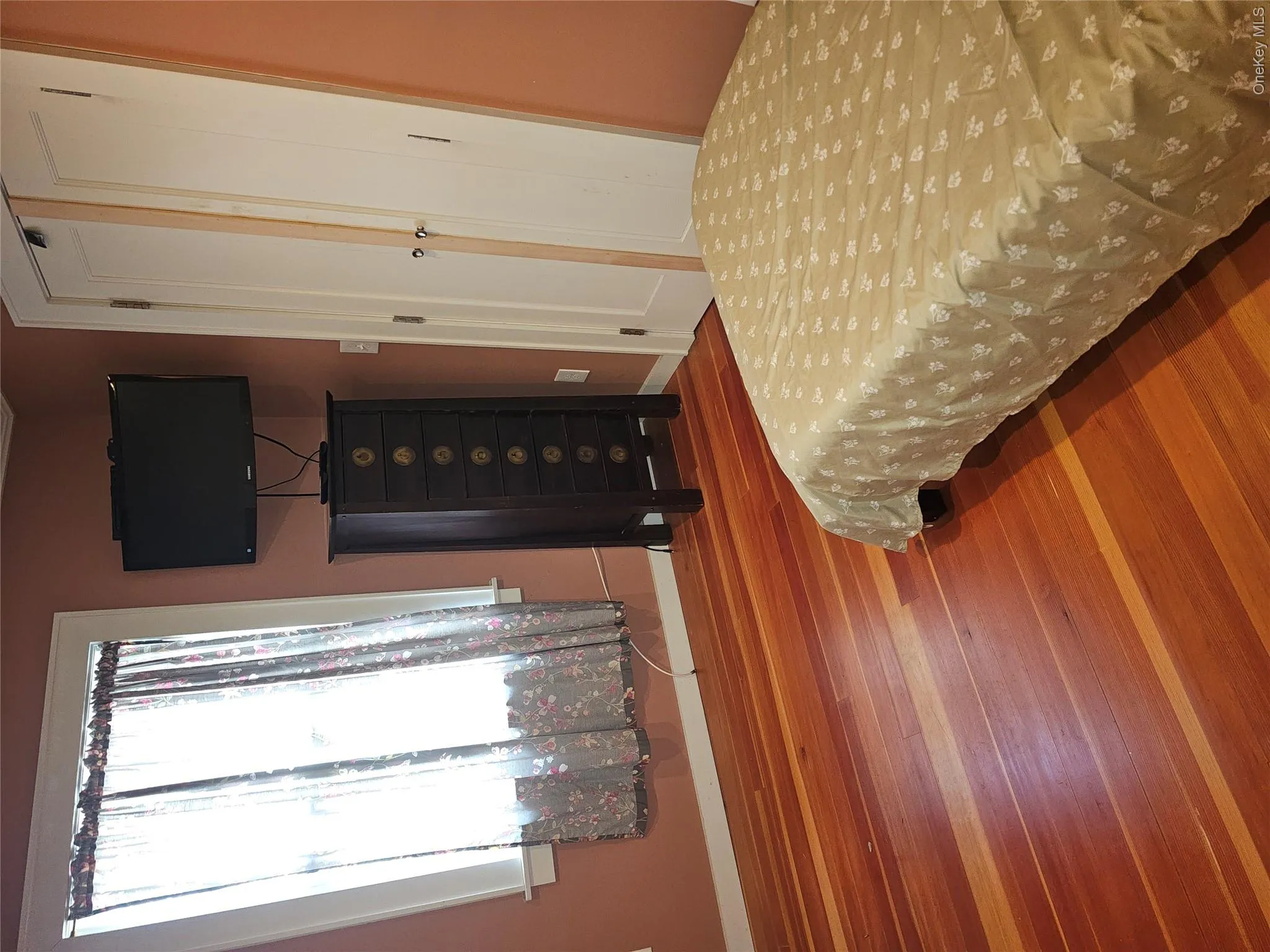 Natural wood-finish flooring, double-panel closet doors with hardware, and a window with white trim Natural wood-finish flooring, double-panel closet doors with hardware, and a window with white trim