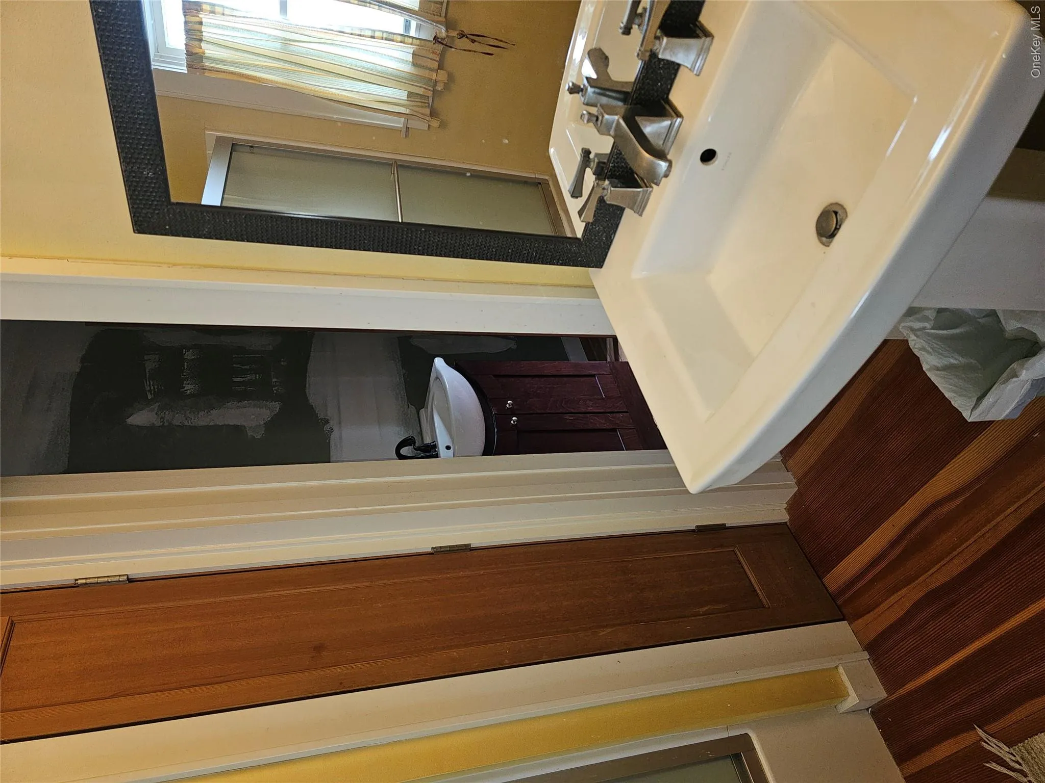 Pedestal sink with polished metal faucet, wood-finish flooring, and framed wall-mounted mirror Pedestal sink with polished metal faucet, wood-finish flooring, and framed wall-mounted mirror