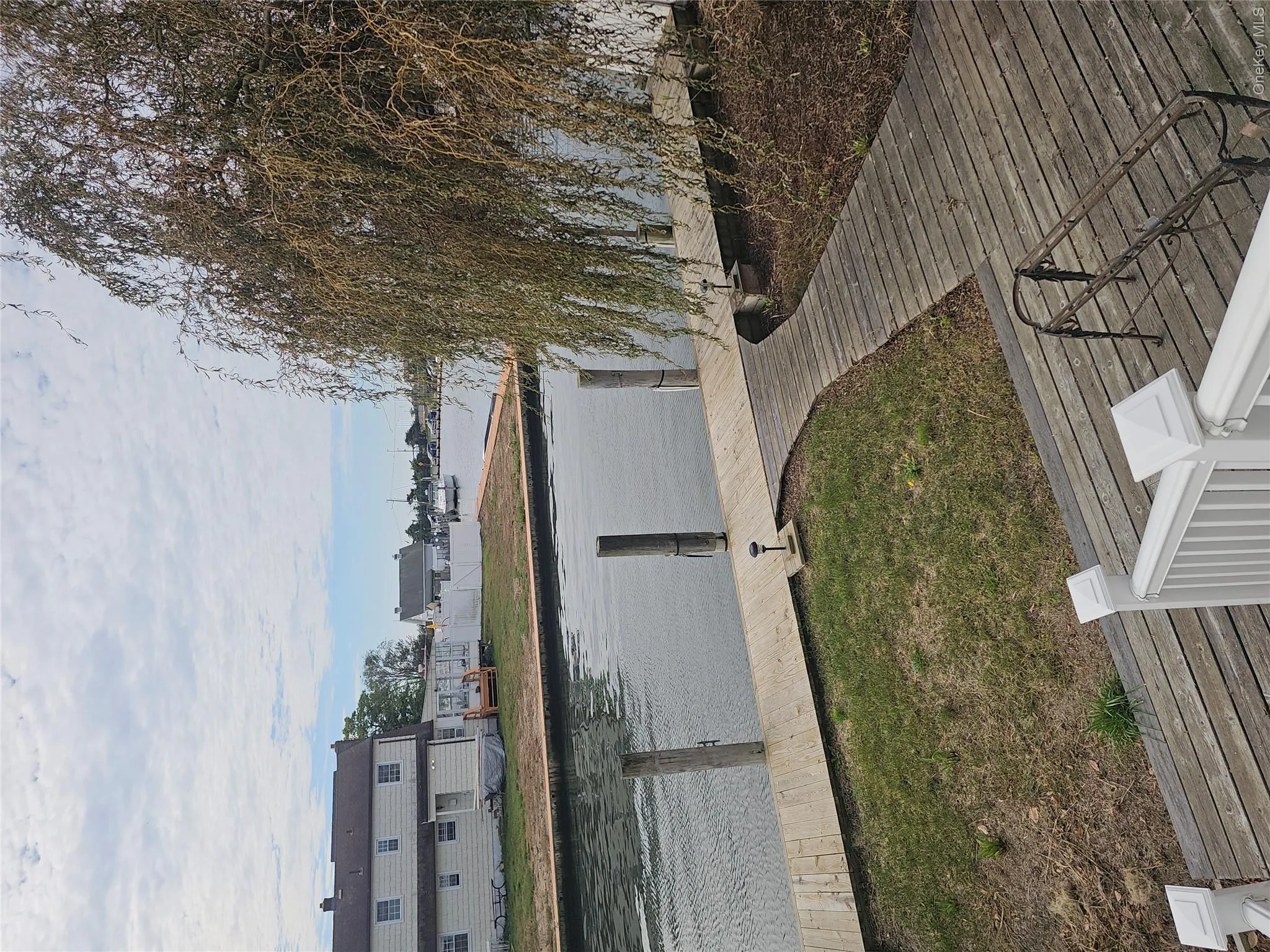 Waterfront property featuring a wood-plank deck, a private bulkhead dock, and mature weeping willow tree Waterfront property featuring a wood-plank deck, a private bulkhead dock, and mature weeping willow tree