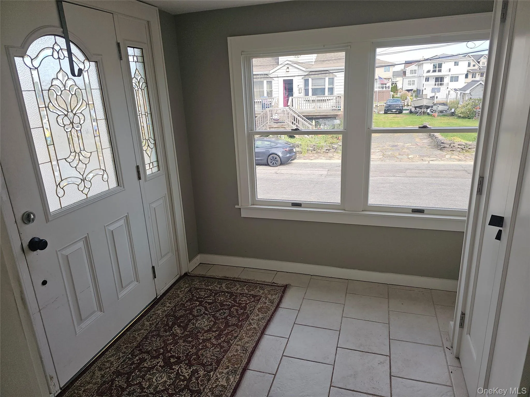 Entryway featuring a white exterior door with decorative glass inserts, ceramic tile flooring, and large windows with white trim Entryway featuring a white exterior door with decorative glass inserts, ceramic tile flooring, and large windows with white trim