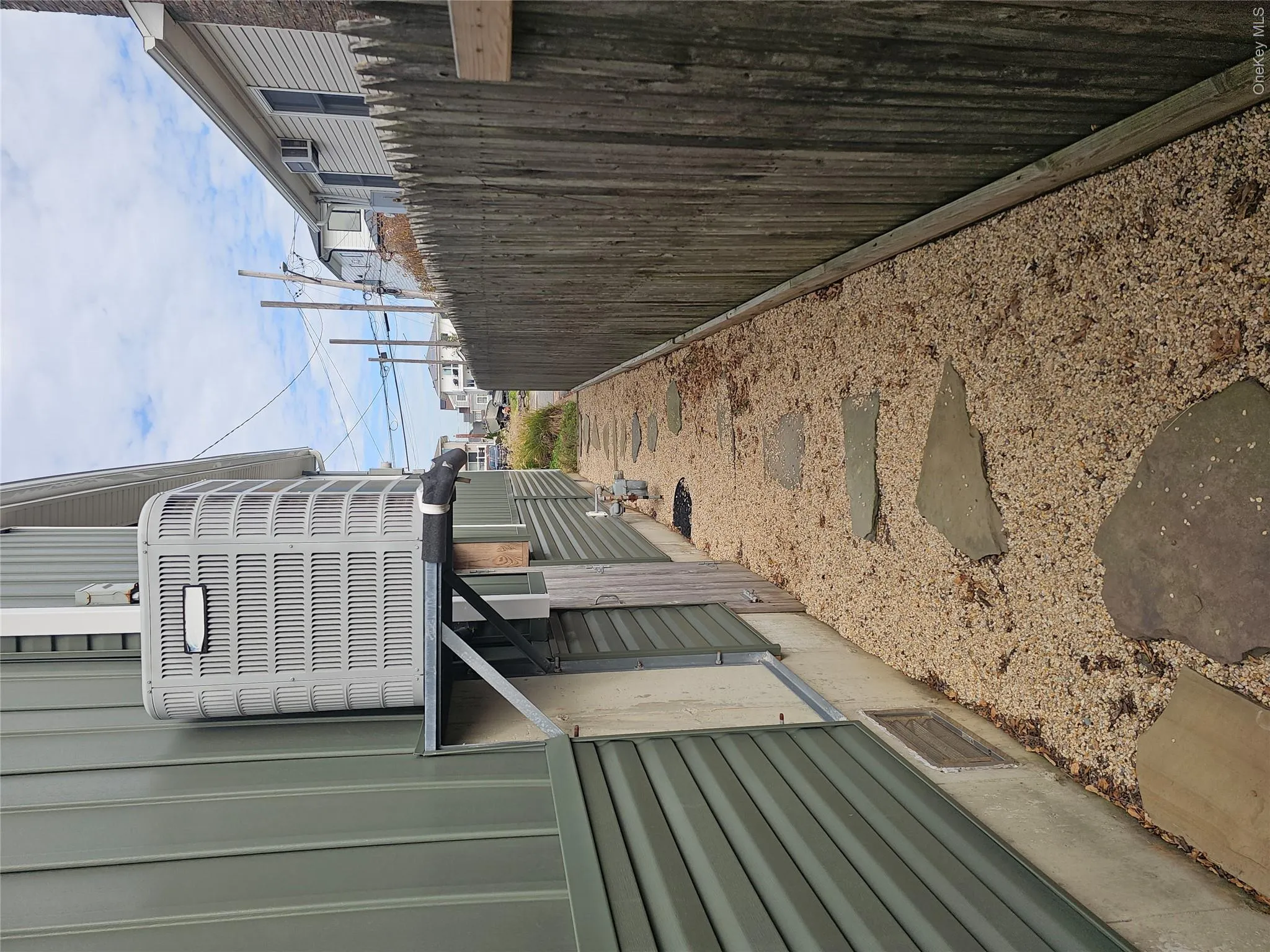 Side yard featuring a gravel path with integrated stone pavers, a tall wood-picket privacy fence, and a wall-mounted exterior HVAC unit Side yard featuring a gravel path with integrated stone pavers, a tall wood-picket privacy fence, and a wall-mounted exterior HVAC unit