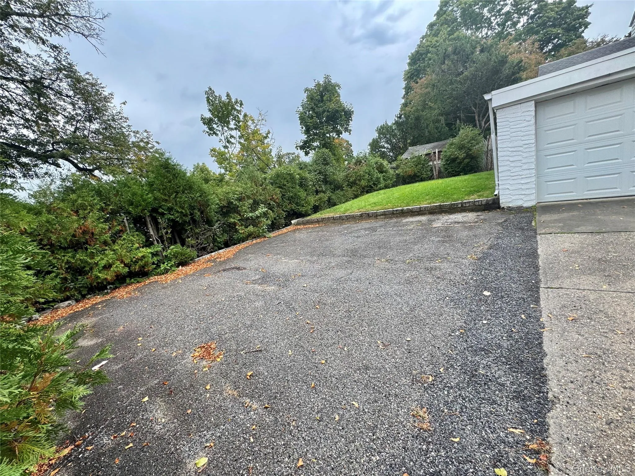 Asphalt driveway with concrete apron, white-painted brick exterior, and tiered landscape retaining wall Asphalt driveway with concrete apron, white-painted brick exterior, and tiered landscape retaining wall