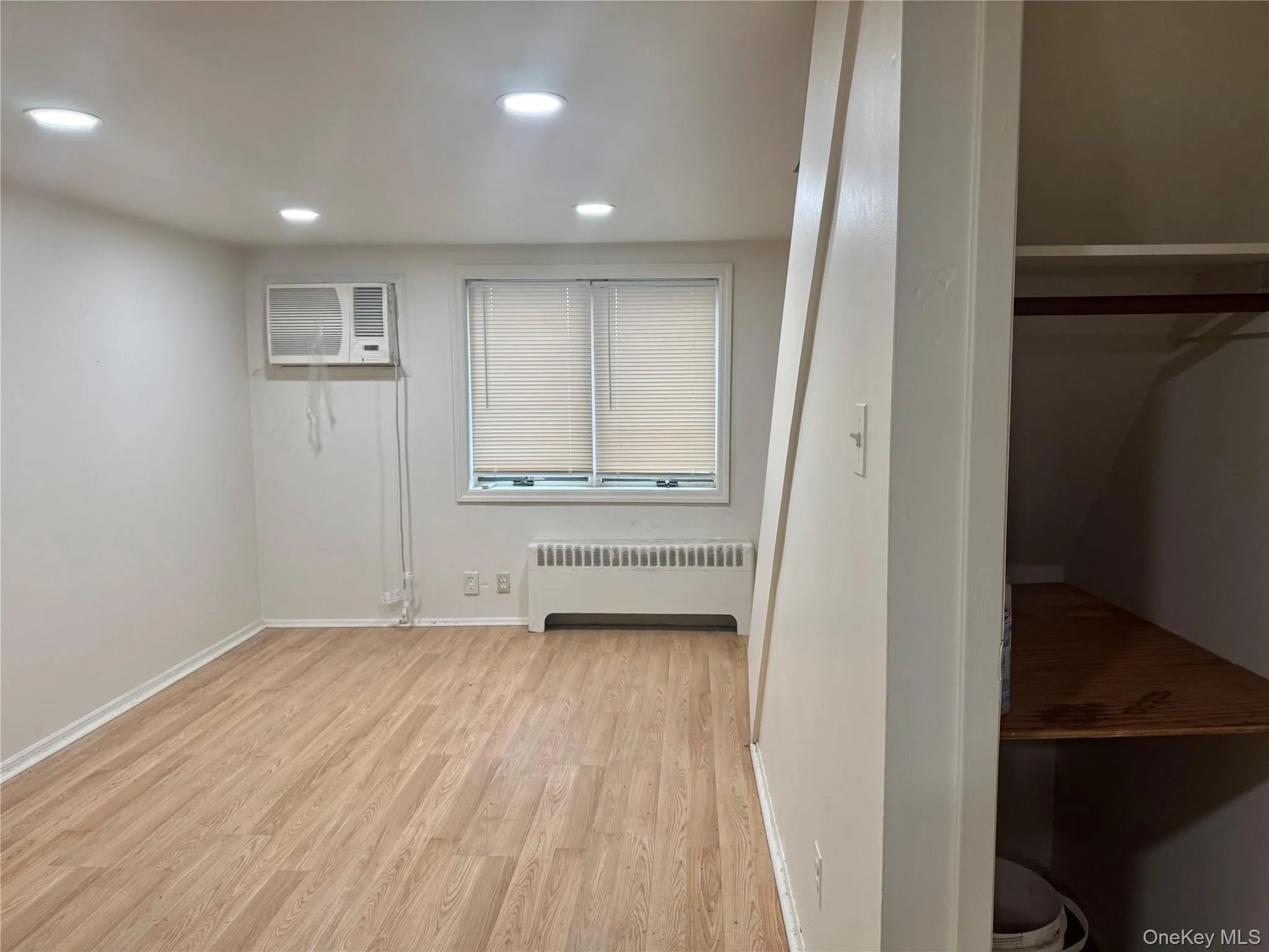 Interior space featuring wood-finish flooring, recessed lighting, wall-mounted air conditioning unit, and built-in closet with integrated shelving Interior space featuring wood-finish flooring, recessed lighting, wall-mounted air conditioning unit, and built-in closet with integrated shelving