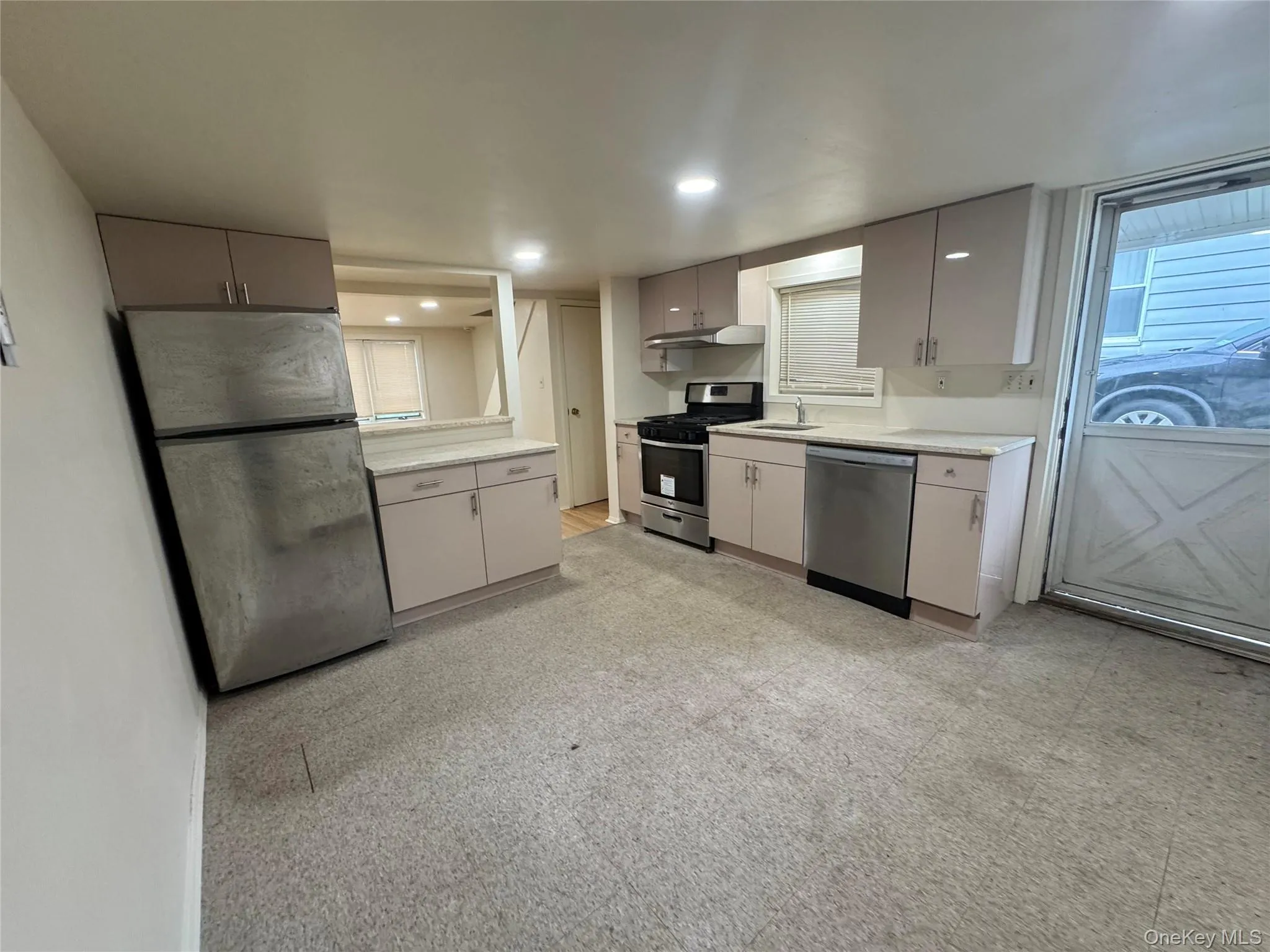 Kitchen featuring light-toned cabinetry, solid surface countertops, stainless steel refrigerator, stainless steel range with integrated hood, and stainless steel dishwasher Kitchen featuring light-toned cabinetry, solid surface countertops, stainless steel refrigerator, stainless steel range with integrated hood, and stainless steel dishwasher
