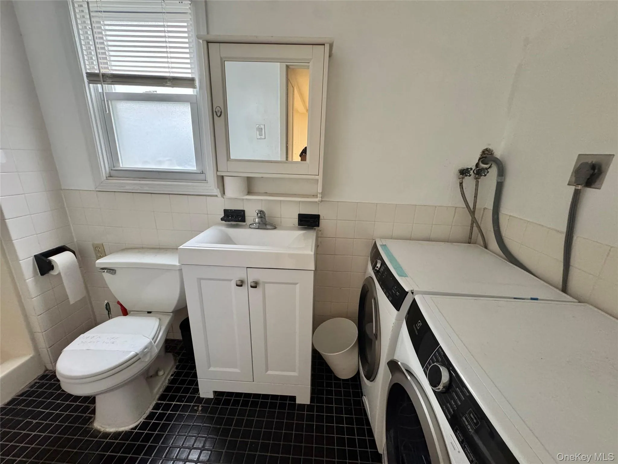 Bathroom featuring a single-door vanity with integrated sink, wall-mounted medicine cabinet, white tiled wall surround, and black grid-pattern flooring Bathroom featuring a single-door vanity with integrated sink, wall-mounted medicine cabinet, white tiled wall surround, and black grid-pattern flooring
