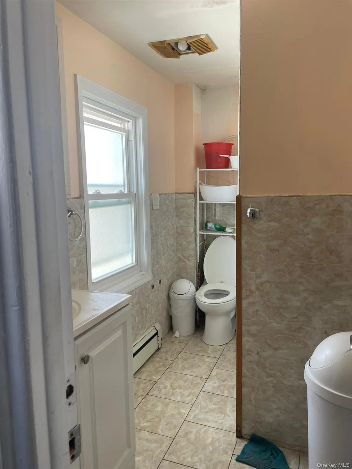 Bathroom featuring toilet, tile walls, vanity, a wainscoted wall, and a baseboard heating unit Bathroom featuring toilet, tile walls, vanity, a wainscoted wall, and a baseboard heating unit