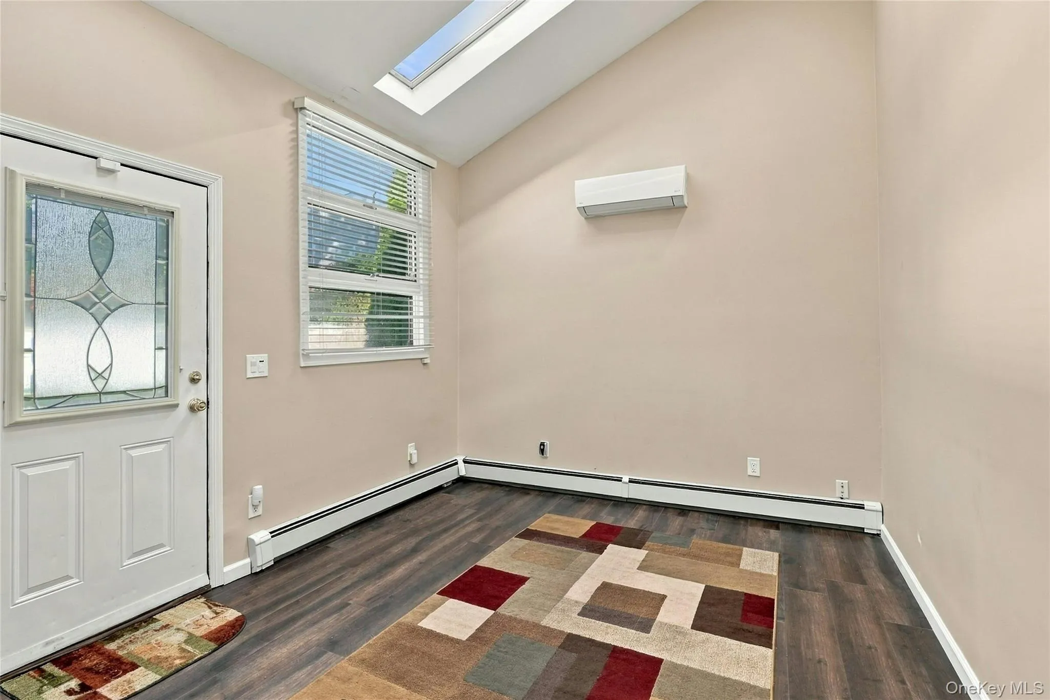 Vaulted ceiling with a skylight, dark wood-finish flooring, energy-efficient mini-split system, and a glass-inset entry door Vaulted ceiling with a skylight, dark wood-finish flooring, energy-efficient mini-split system, and a glass-inset entry door