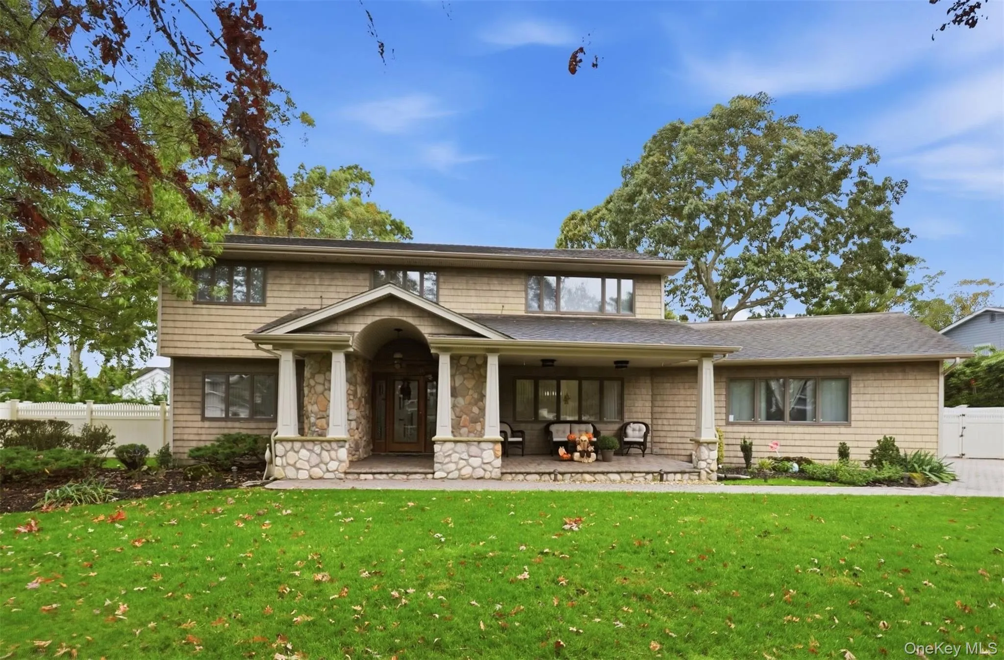 Two-story shingle-style exterior featuring a covered front porch with stone pillars, a stone-accented entryway, and a paved walkway Two-story shingle-style exterior featuring a covered front porch with stone pillars, a stone-accented entryway, and a paved walkway