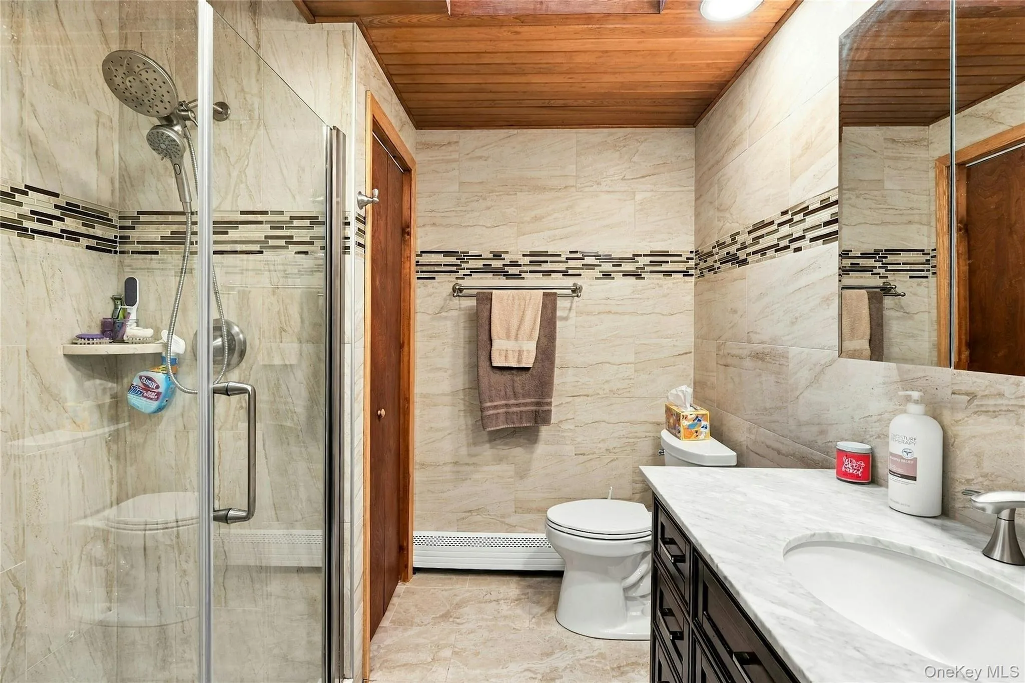 Bathroom featuring a walk-in shower with glass enclosure, wood-paneled ceiling, stone-finish wall tile with mosaic accent inlay, and vanity with stone-finish countertop Bathroom featuring a walk-in shower with glass enclosure, wood-paneled ceiling, stone-finish wall tile with mosaic accent inlay, and vanity with stone-finish countertop