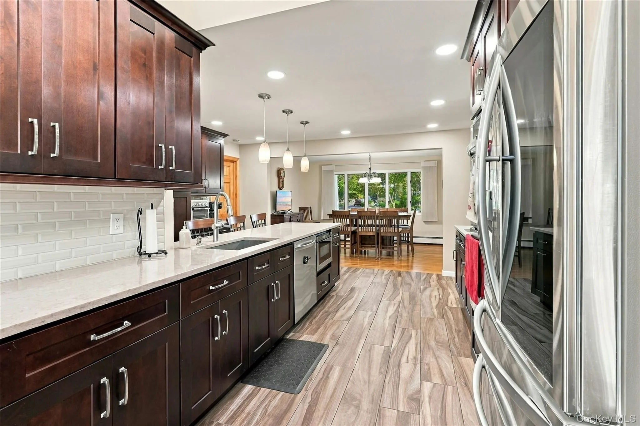 Kitchen featuring stained wood cabinetry, stone countertops, white subway tile backsplash, wood-finish flooring, and stainless steel appliances Kitchen featuring stained wood cabinetry, stone countertops, white subway tile backsplash, wood-finish flooring, and stainless steel appliances