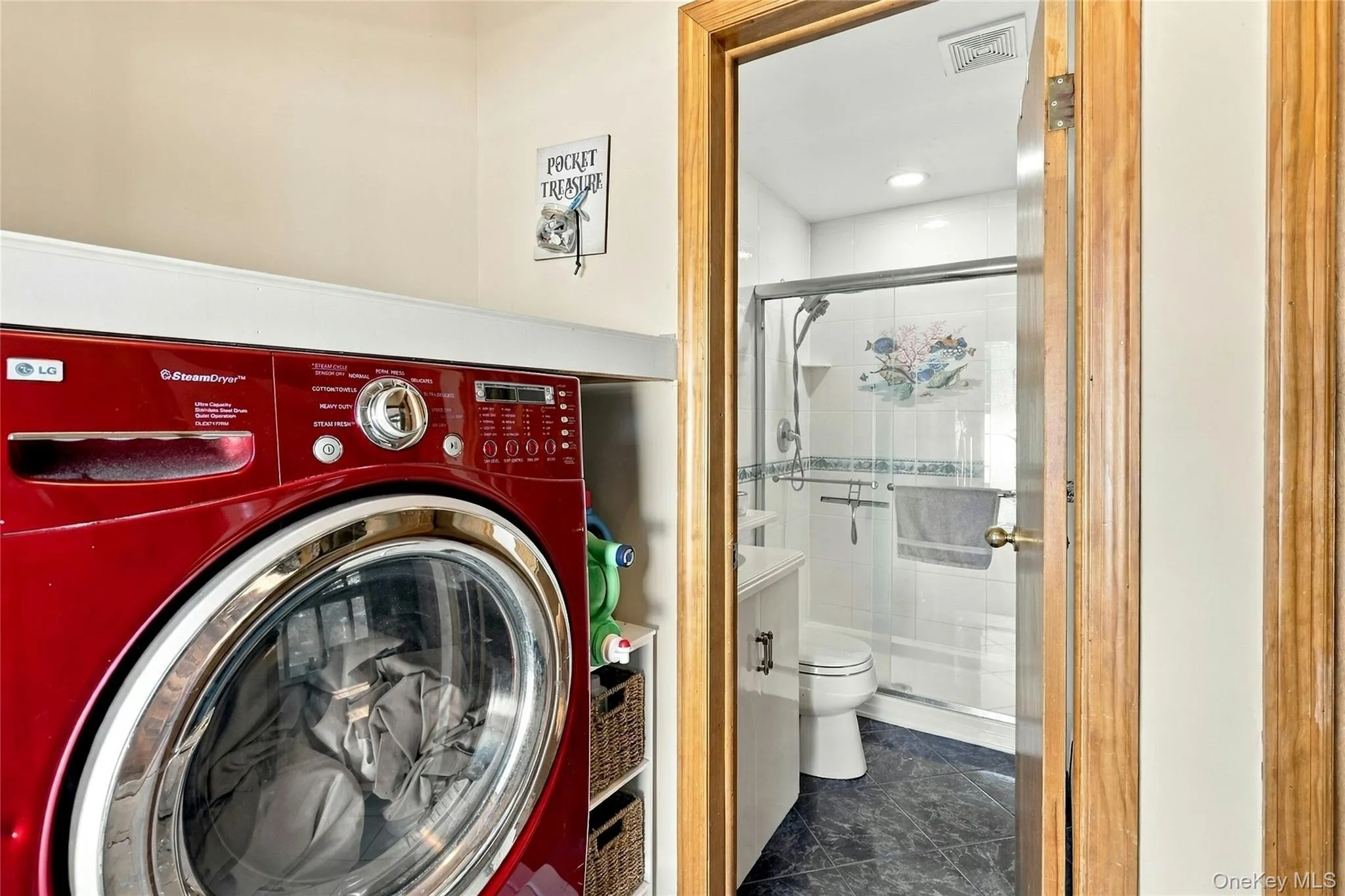 Laundry area featuring a built-in shelf and cabinetry, paired with a bathroom containing a walk-in shower with glass enclosure, tile surround, and dark-toned flooring Laundry area featuring a built-in shelf and cabinetry, paired with a bathroom containing a walk-in shower with glass enclosure, tile surround, and dark-toned flooring