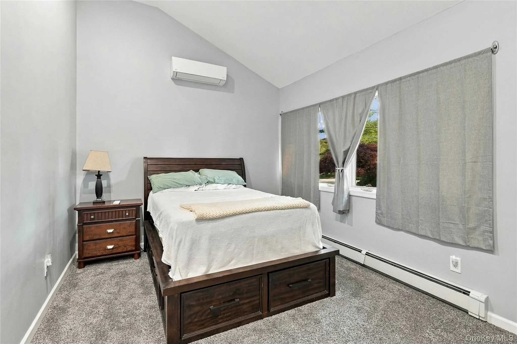 Vaulted ceilings featuring a wall-mounted ductless heating and cooling unit, neutral carpeting, and a window with hardware Vaulted ceilings featuring a wall-mounted ductless heating and cooling unit, neutral carpeting, and a window with hardware