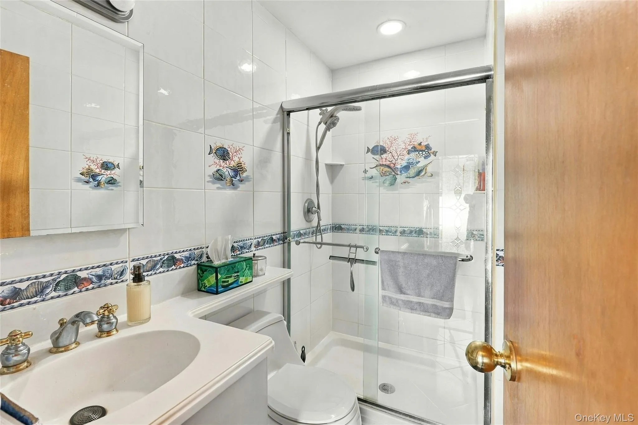 Full bathroom featuring a white vanity with an integrated sink, polished metal fixtures, a shower enclosure with sliding glass doors, and a handheld showerhead Full bathroom featuring a white vanity with an integrated sink, polished metal fixtures, a shower enclosure with sliding glass doors, and a handheld showerhead