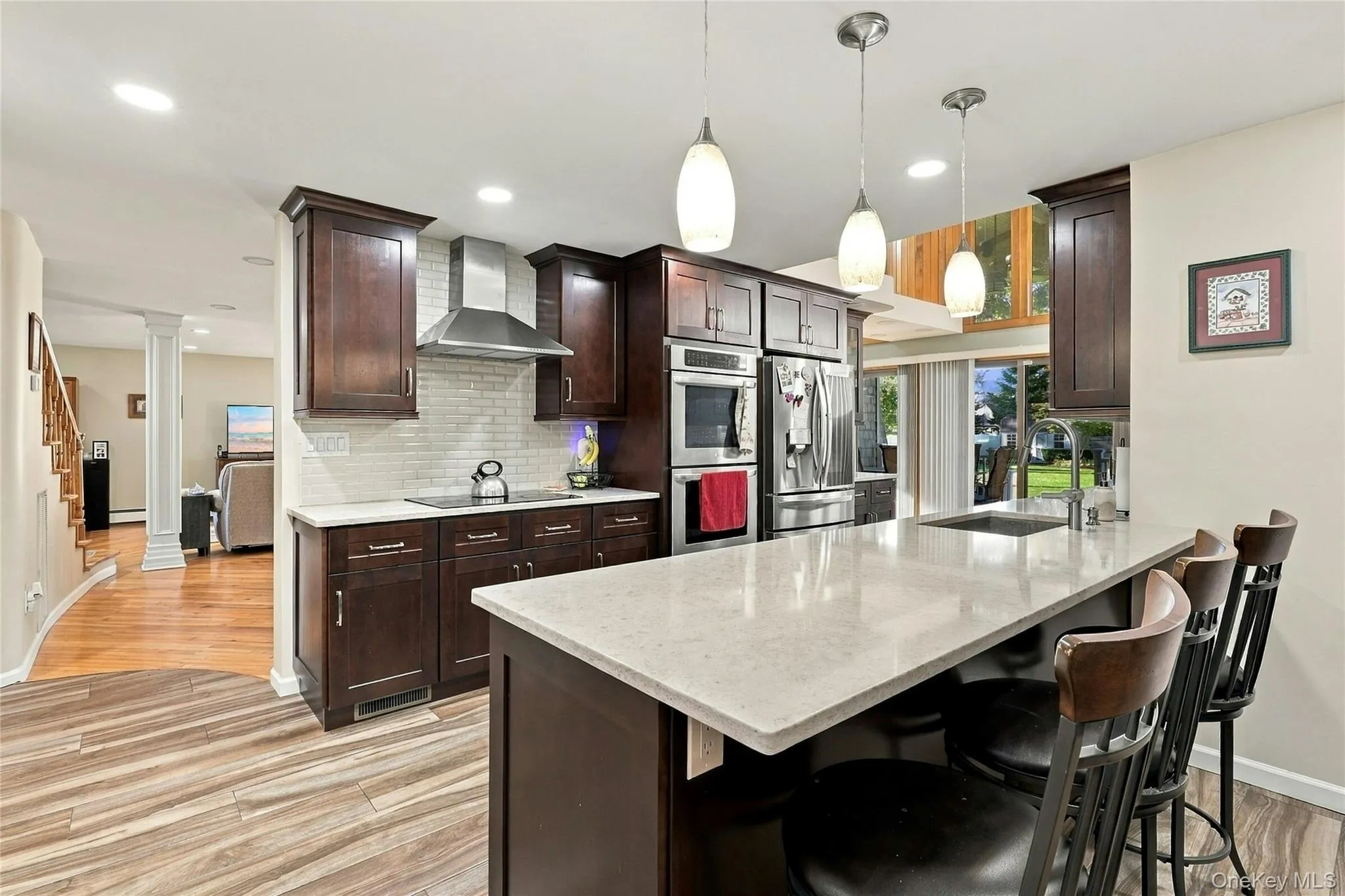 Kitchen featuring dark wood cabinetry, quartz countertops, a central island with a stainless steel undermount sink, subway tile backsplash, and built-in stainless steel appliances Kitchen featuring dark wood cabinetry, quartz countertops, a central island with a stainless steel undermount sink, subway tile backsplash, and built-in stainless steel appliances